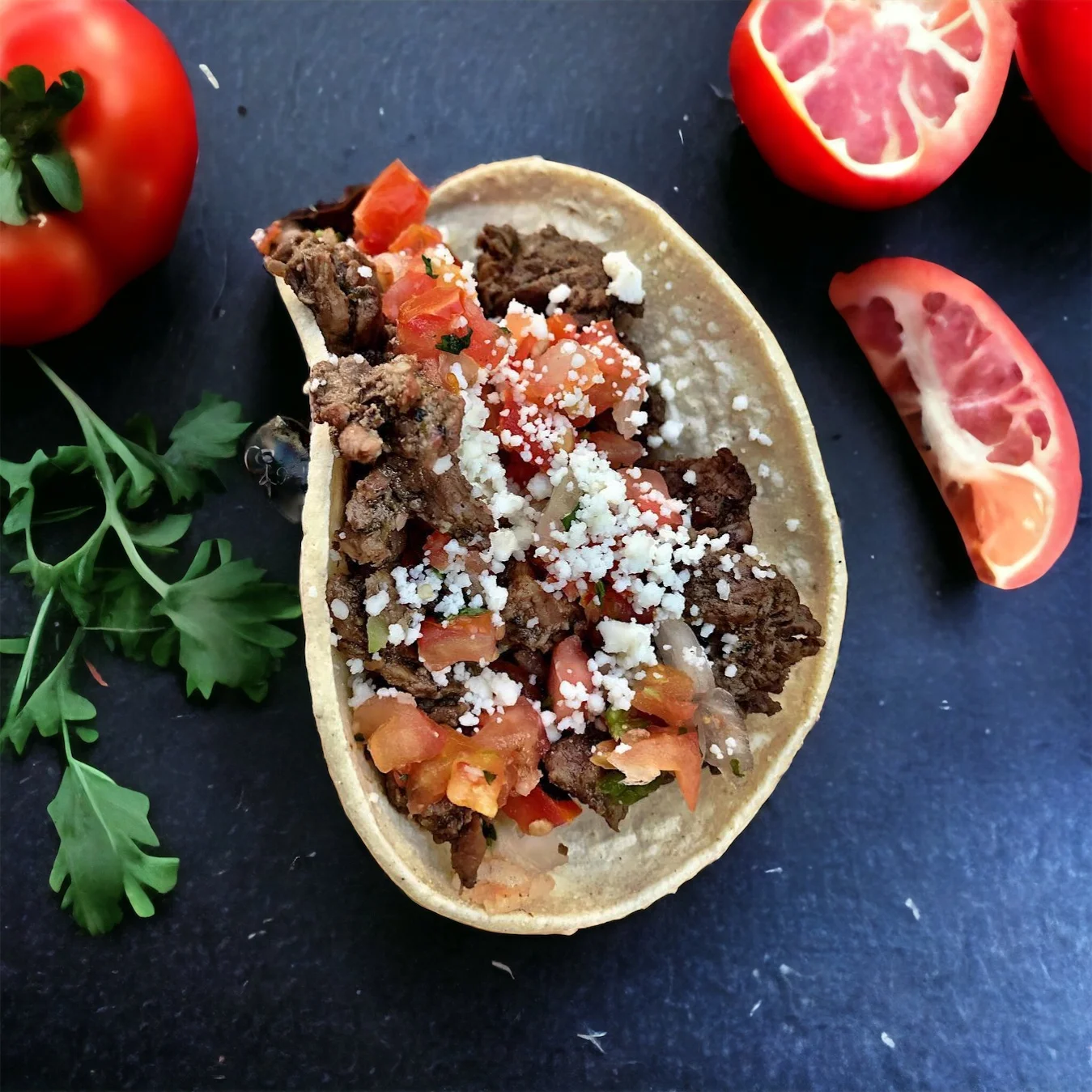 A close-up of a taco filled with beef, diced tomatoes, and crumbled cheese, accompanied by fresh tomatoes and cilantro on the side.