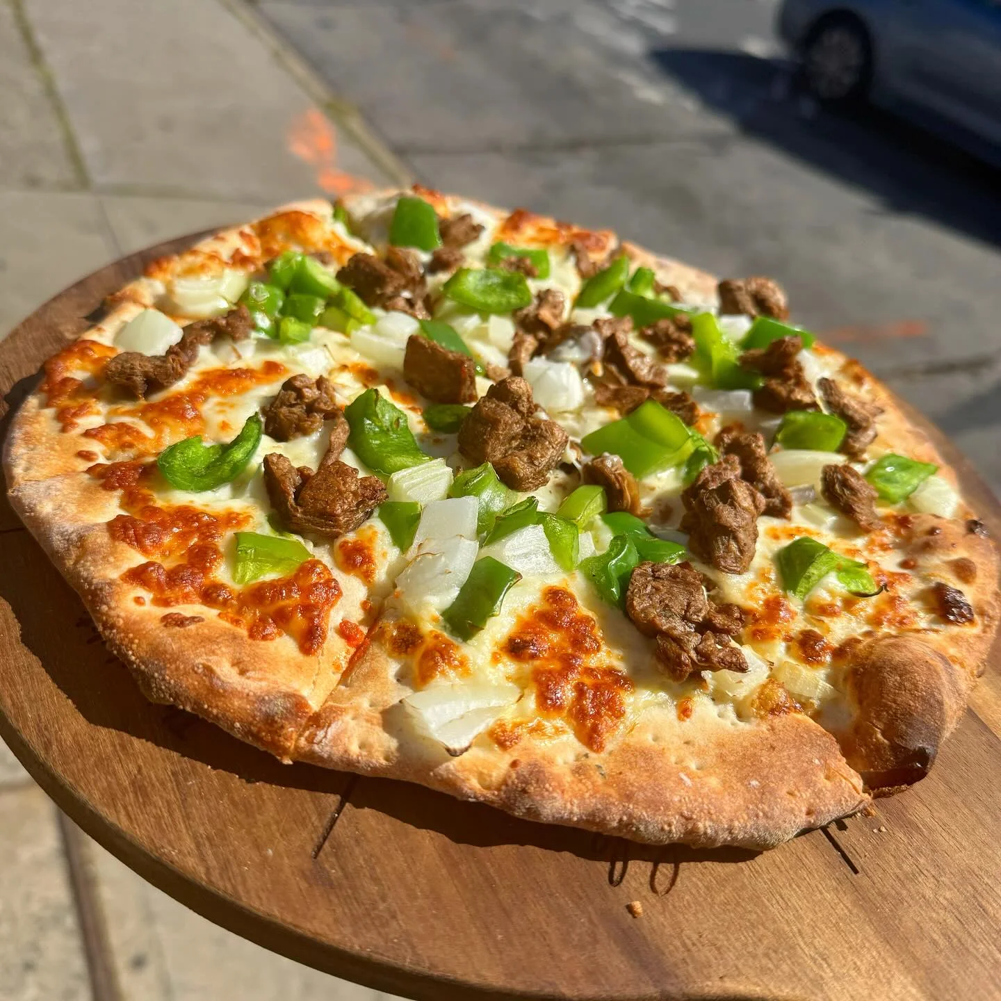 A pizza topped with chunks of meat, green bell peppers, and onions, served on a wooden board.