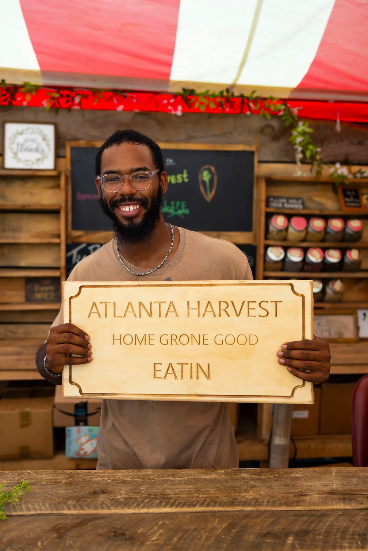 Smiling vendor holding a sign for Atlanta Harvest at a market