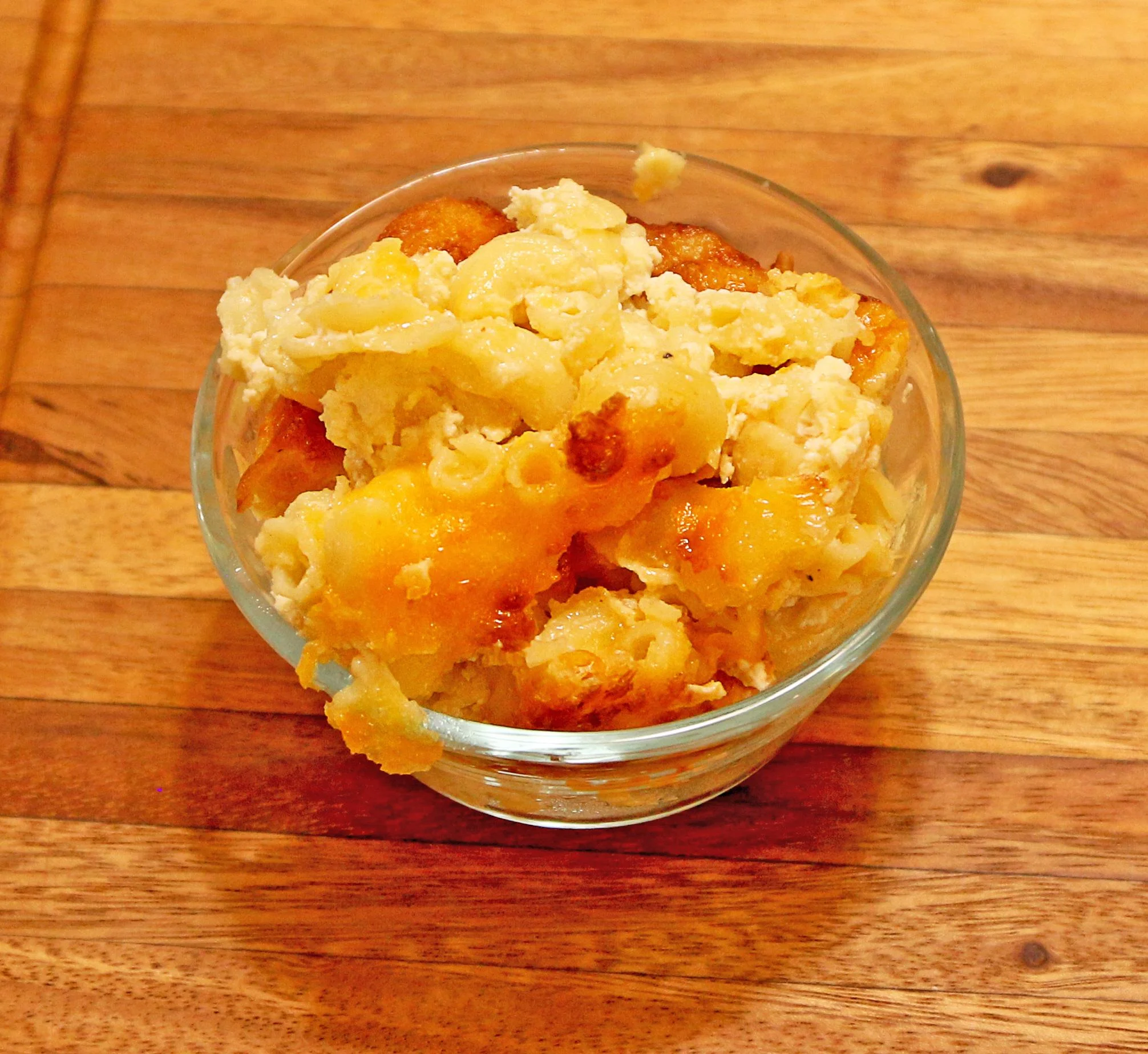 A serving of baked macaroni and cheese in a glass bowl, featuring a golden-brown top and creamy texture.