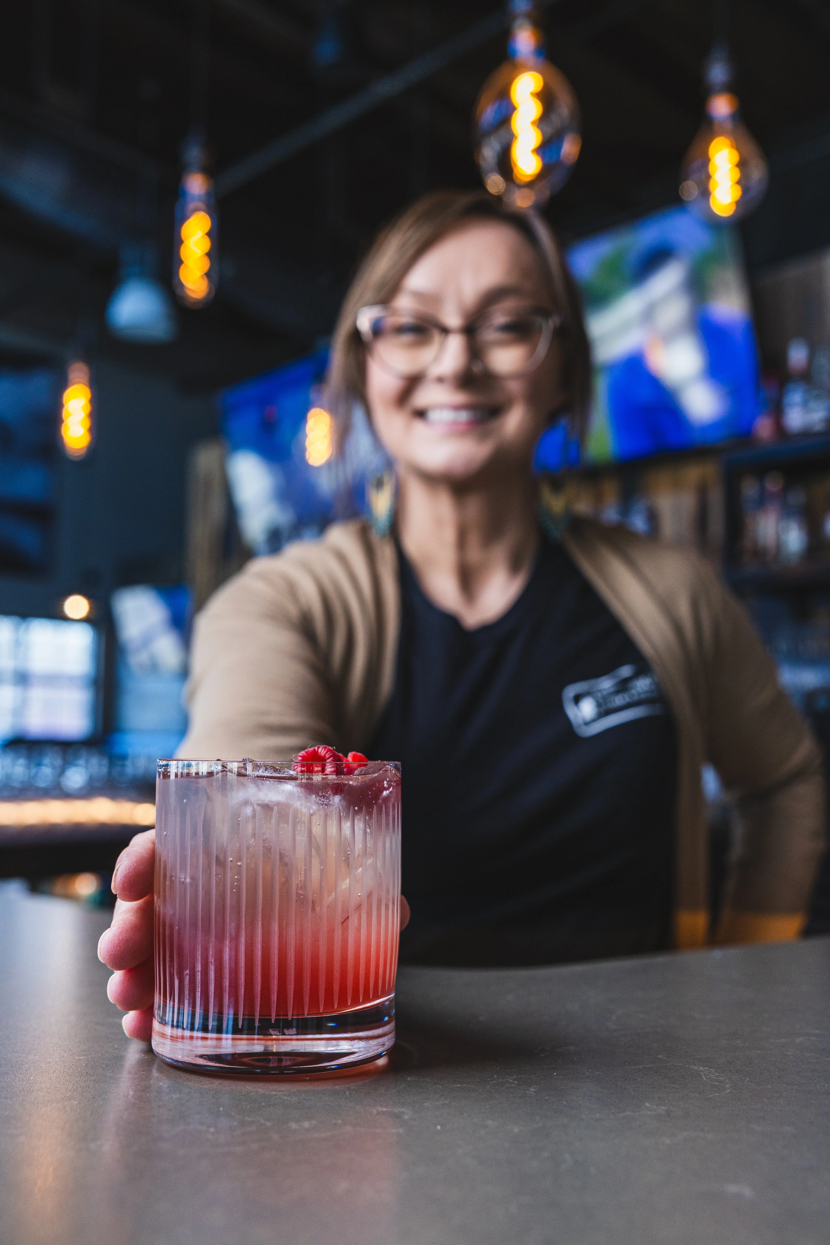 Bartender serving a colorful cocktail with raspberries at a bar.