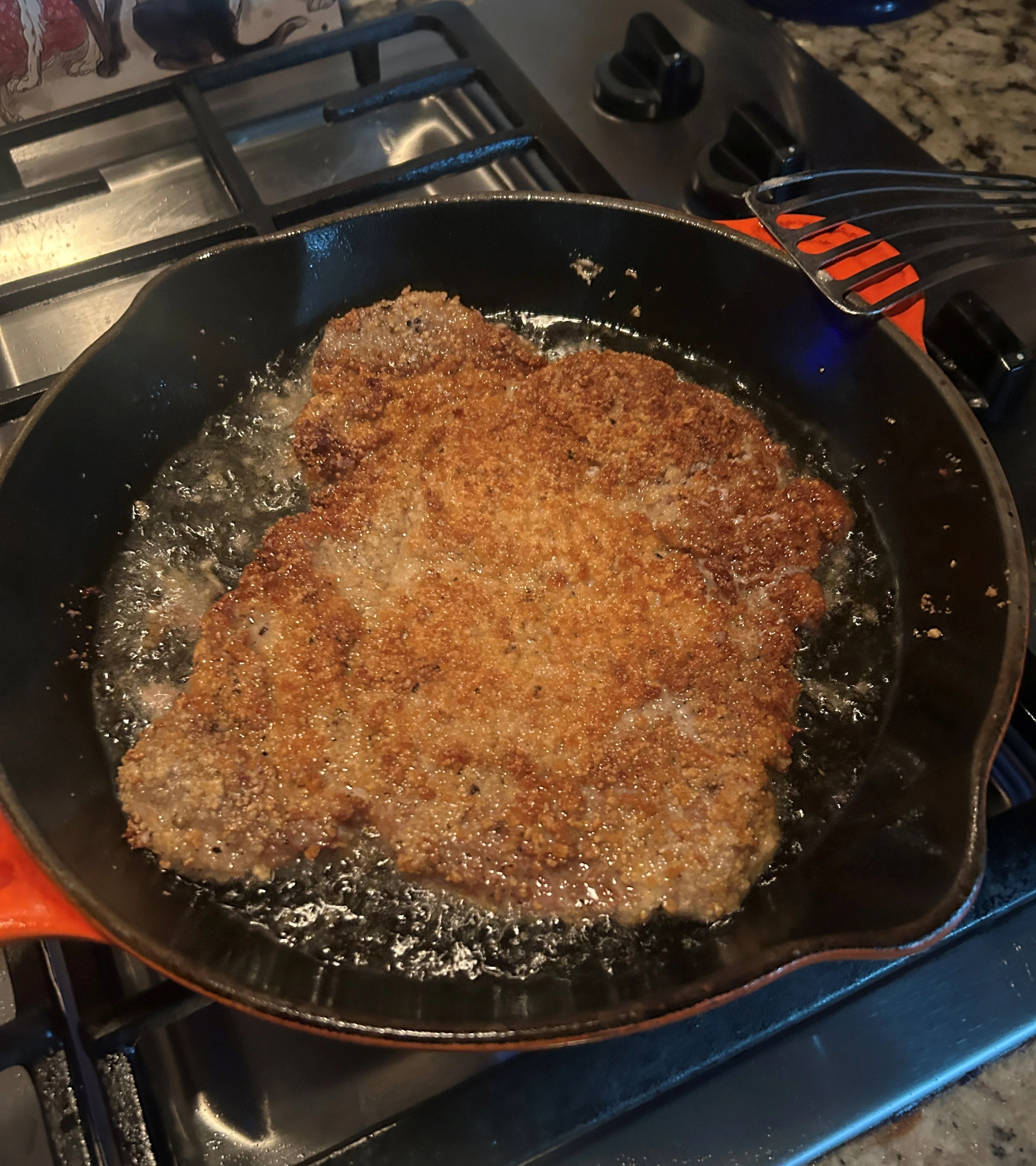 Crispy chicken schnitzel frying in a cast iron skillet