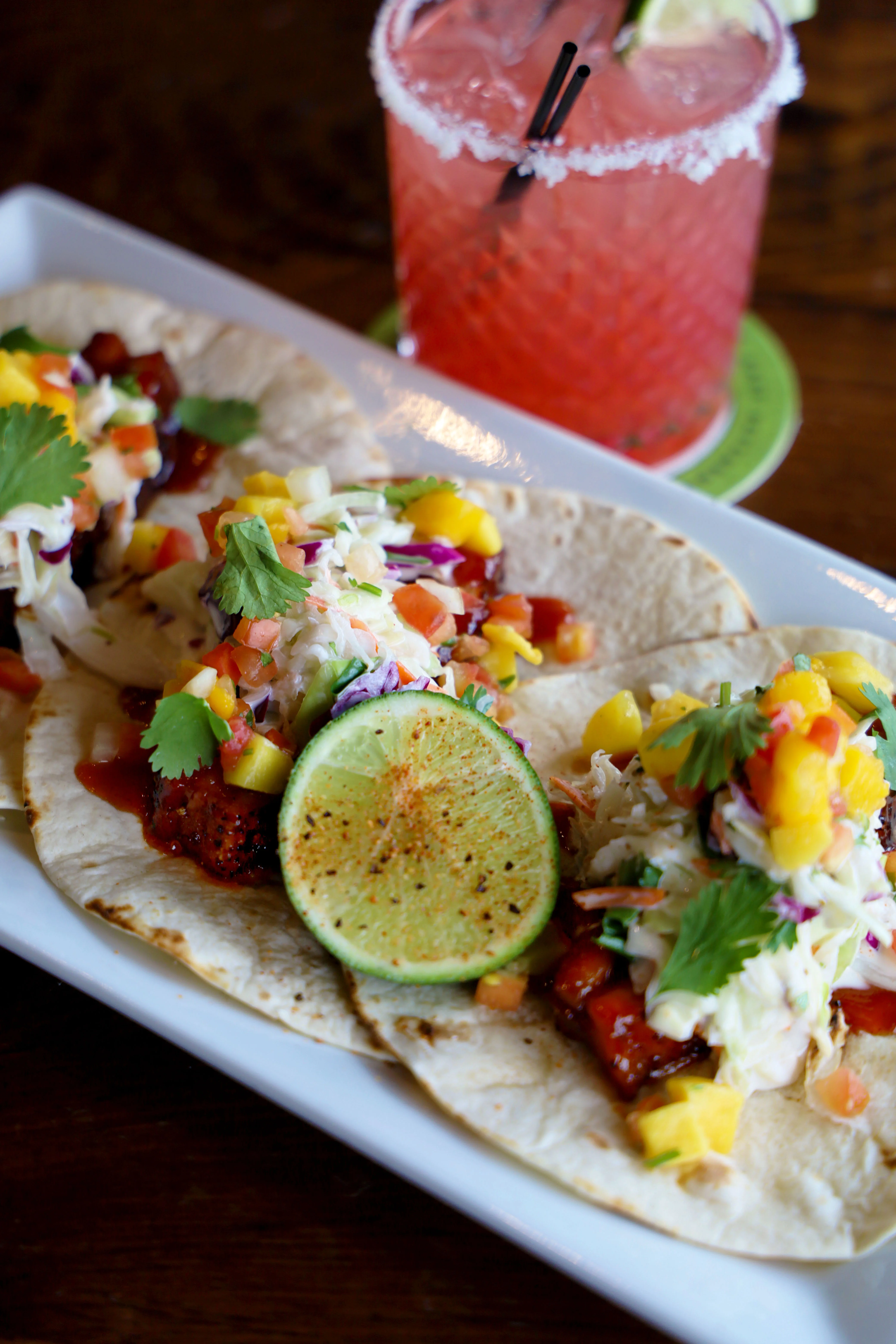 Three tacos with pulled meat, pineapple, and lime on a plate.