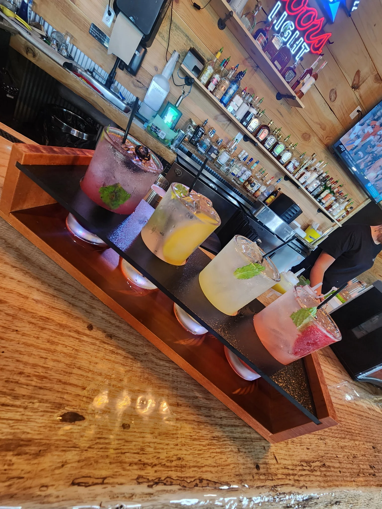 Colorful cocktails served on a wooden tray at a lively bar