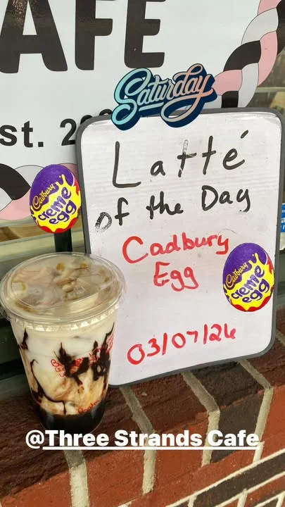 A chalkboard sign advertising the 'Latte of the Day' featuring a Cadbury Egg, next to a clear cup with a layered drink.