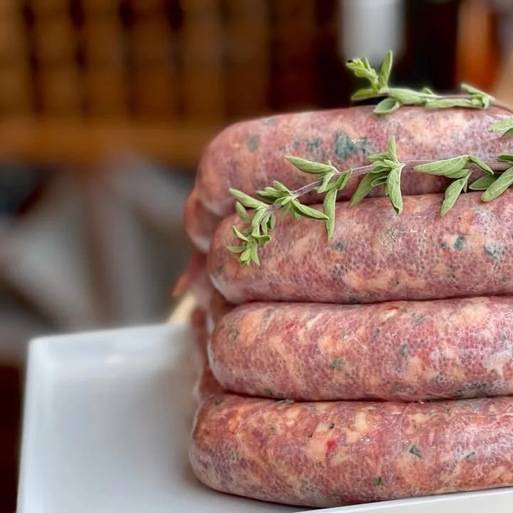 A stack of freshly made sausages garnished with herbs displayed on a white plate.
