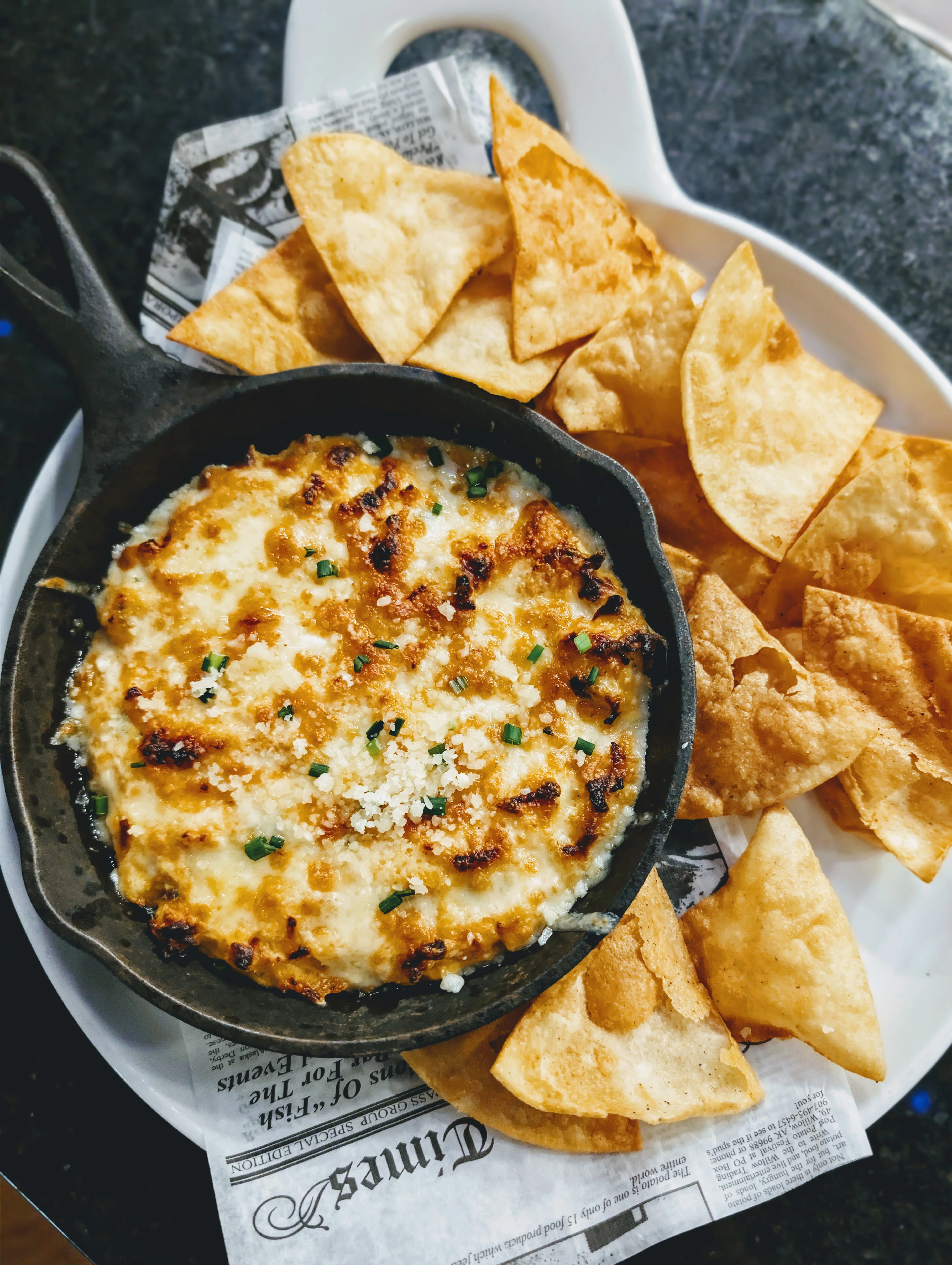 A sizzling cast iron skillet filled with baked cheese dip, served with crispy tortilla chips on the side.