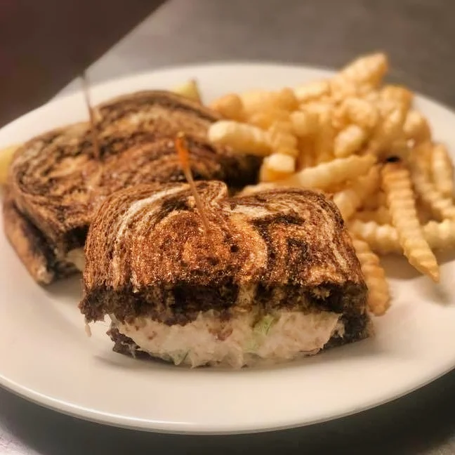 A toasted tuna sandwich with a creamy filling, served with a side of golden crinkle-cut fries on a white plate.