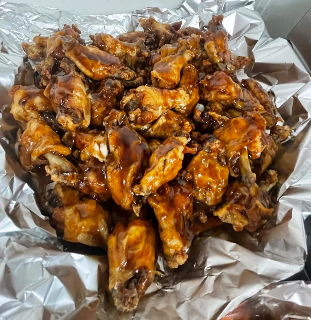 A serving of glazed chicken wings piled high on a sheet of aluminum foil.