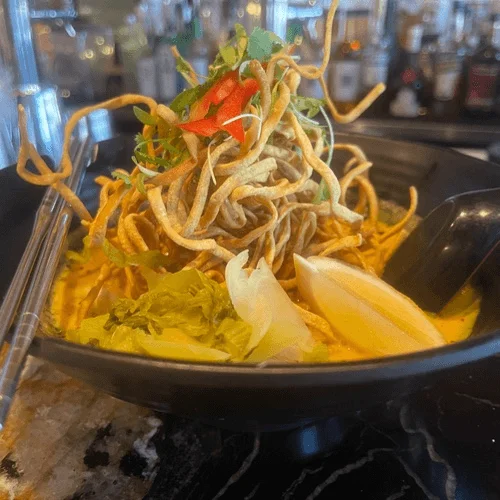 Bowl of Burmese khow suey with crispy noodles and fresh herbs