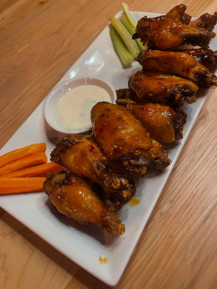 A plate of crispy chicken wings glazed with sauce, accompanied by a side of ranch dressing and sticks of celery and carrot.