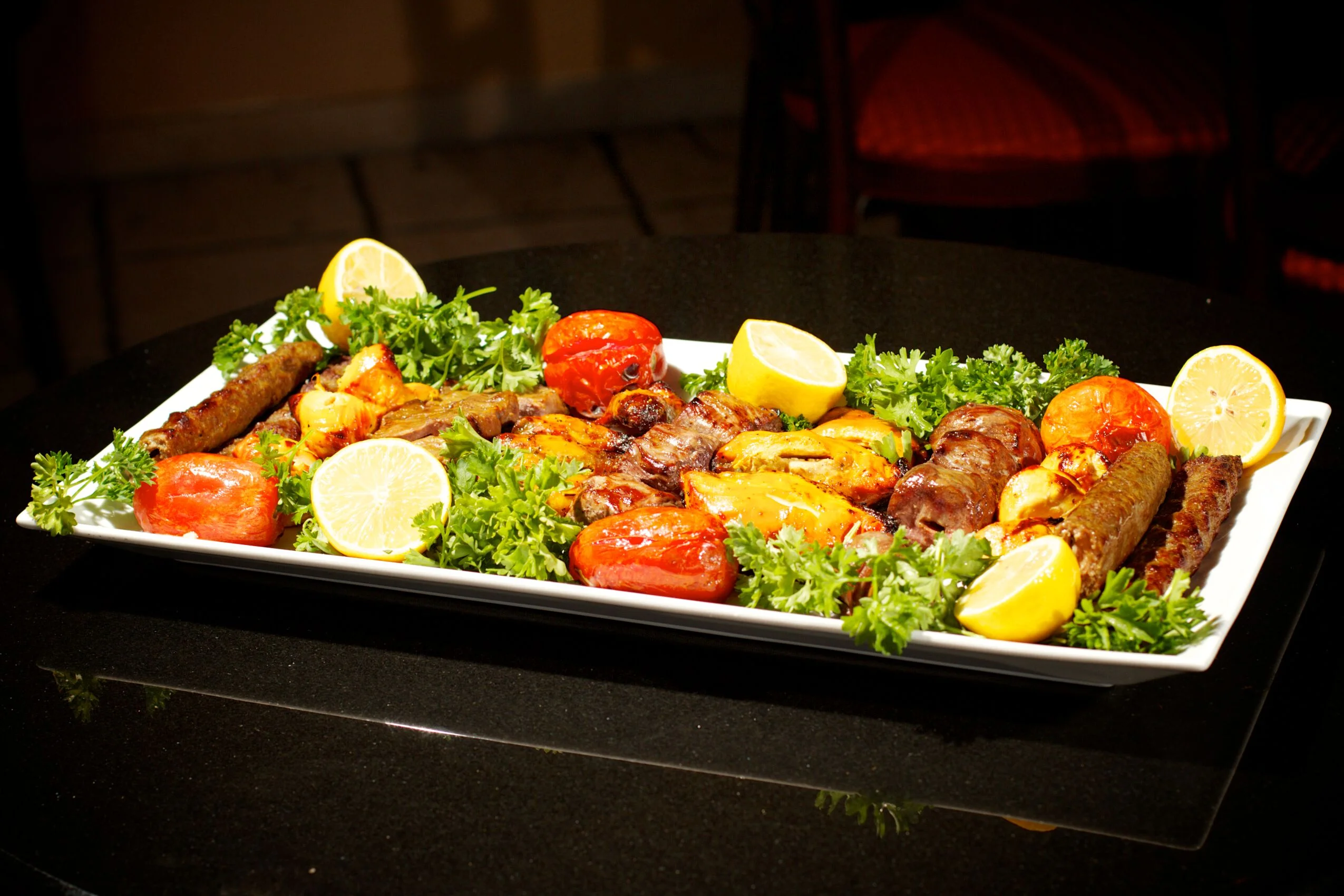 A large serving platter featuring assorted grilled meats, vegetables, and garnishes, including lemon and parsley.