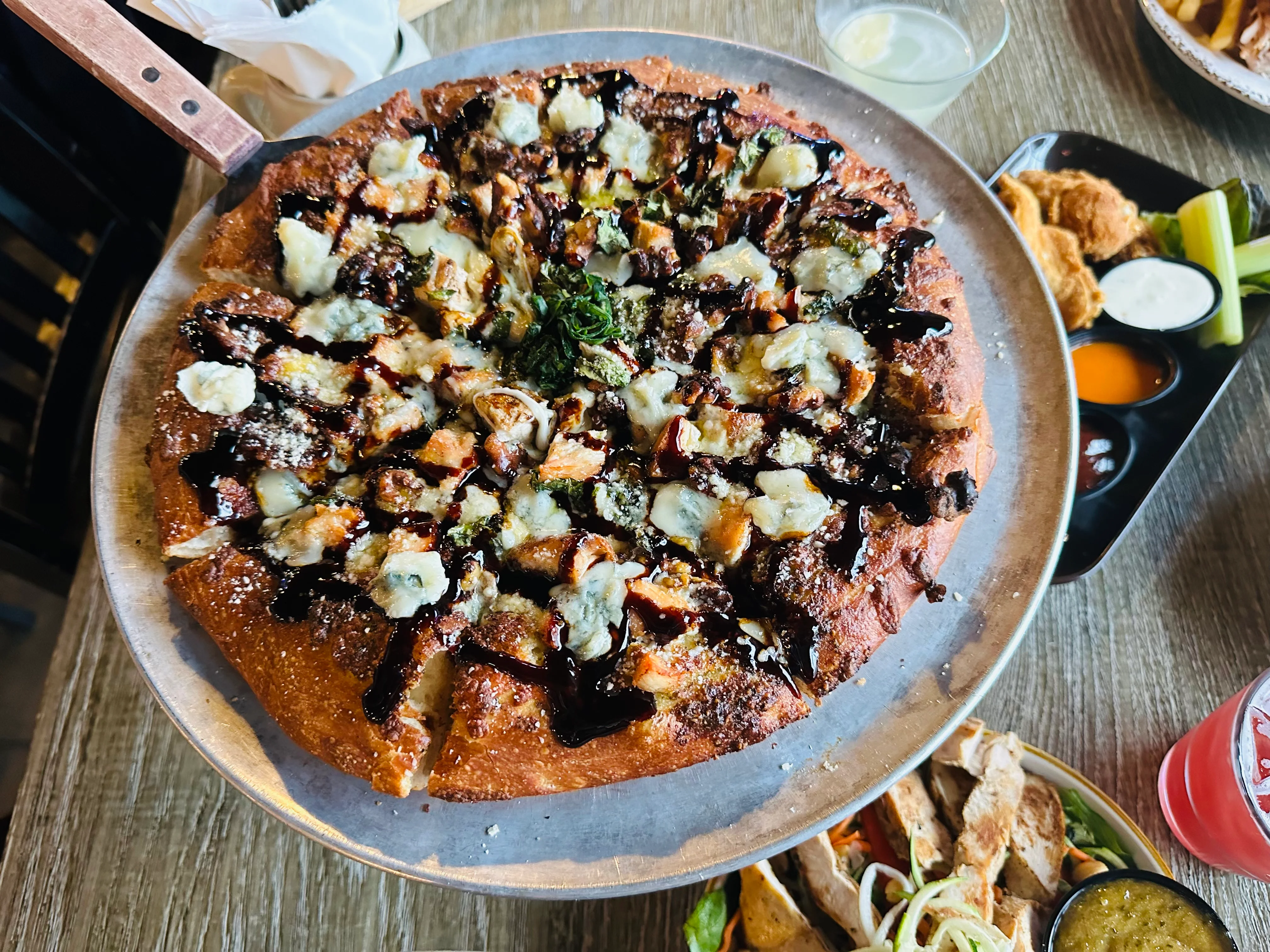 A gourmet pizza topped with a variety of ingredients and drizzled with sauce, served on a metal platter.