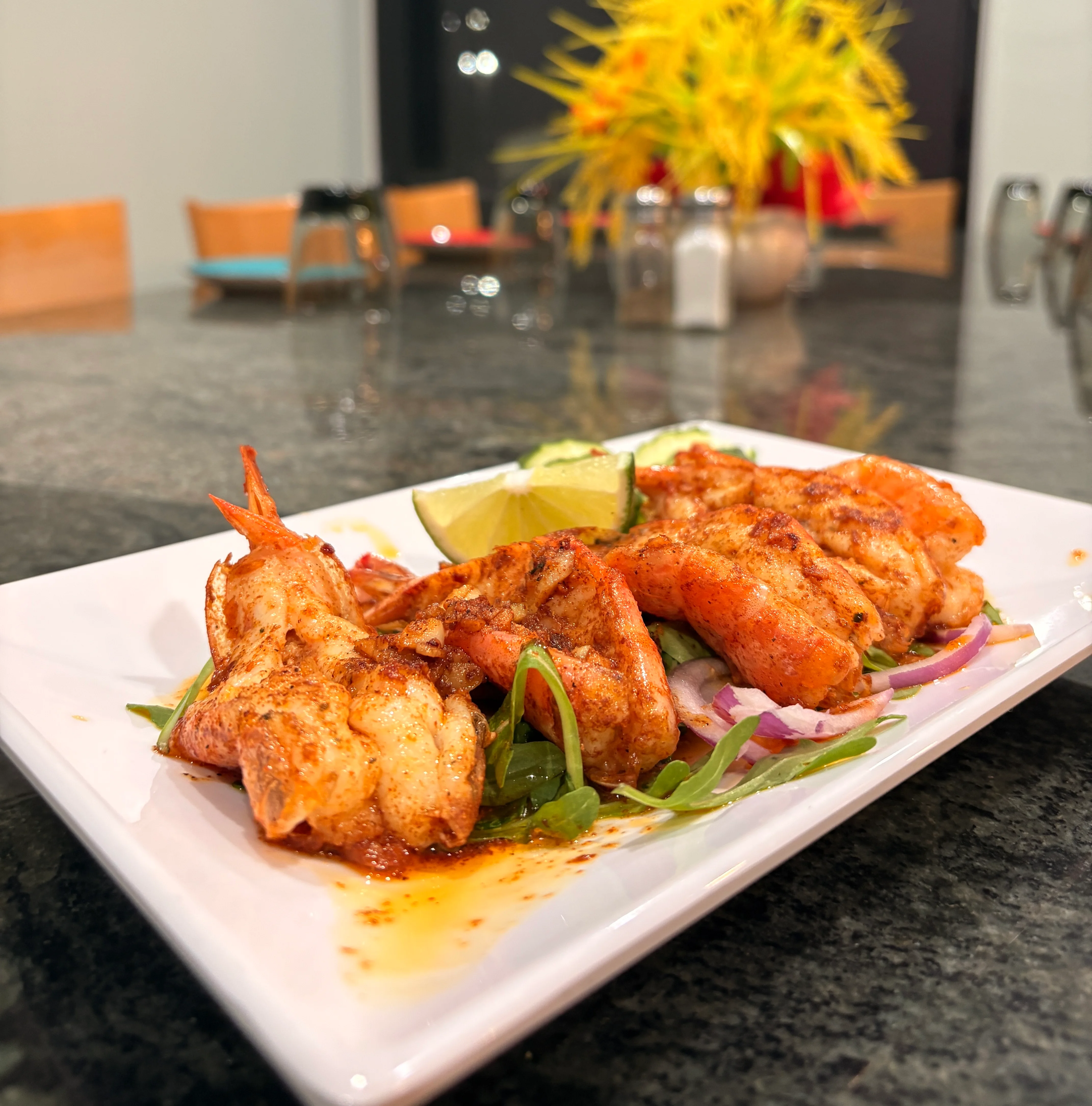 A plate of spicy grilled shrimp served on a bed of greens, garnished with lime and red onion.