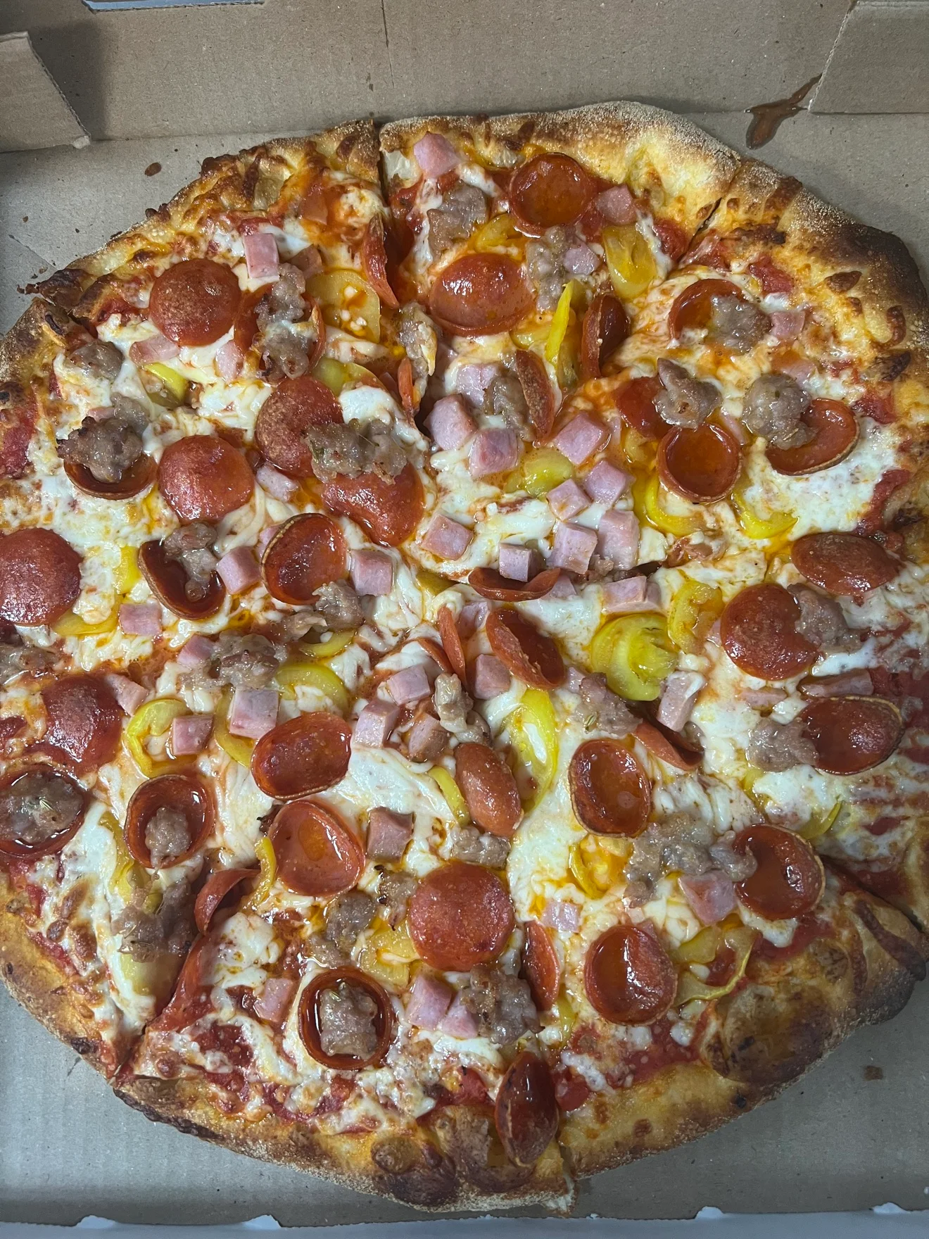 Loaded American-style pepperoni pizza in a cardboard delivery box
