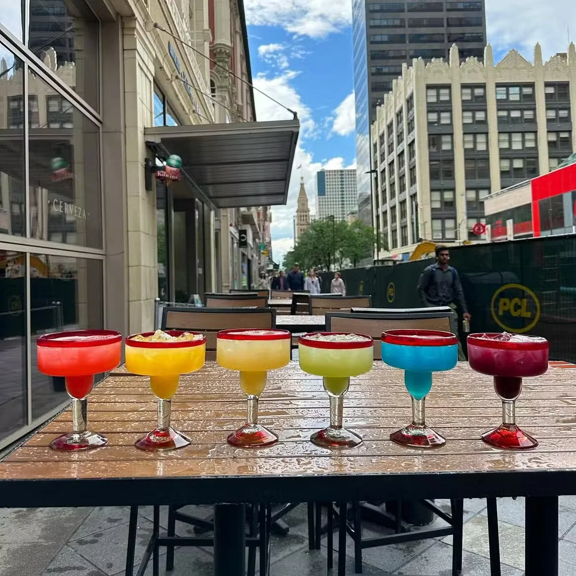 Colorful margaritas on a table outside a restaurant on a sunny day.