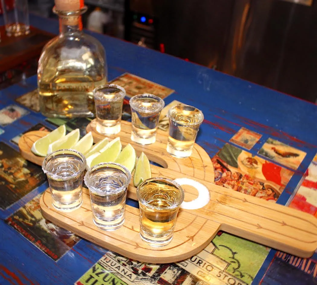 Tequila shots served with lime wedges on a wooden platter