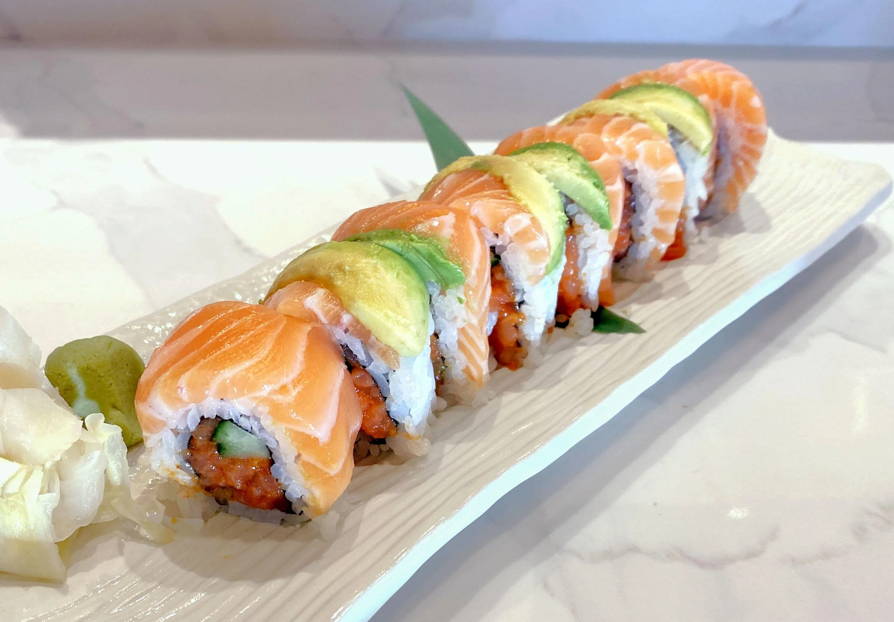 A sushi roll featuring layers of salmon and avocado, beautifully arranged on a white plate.