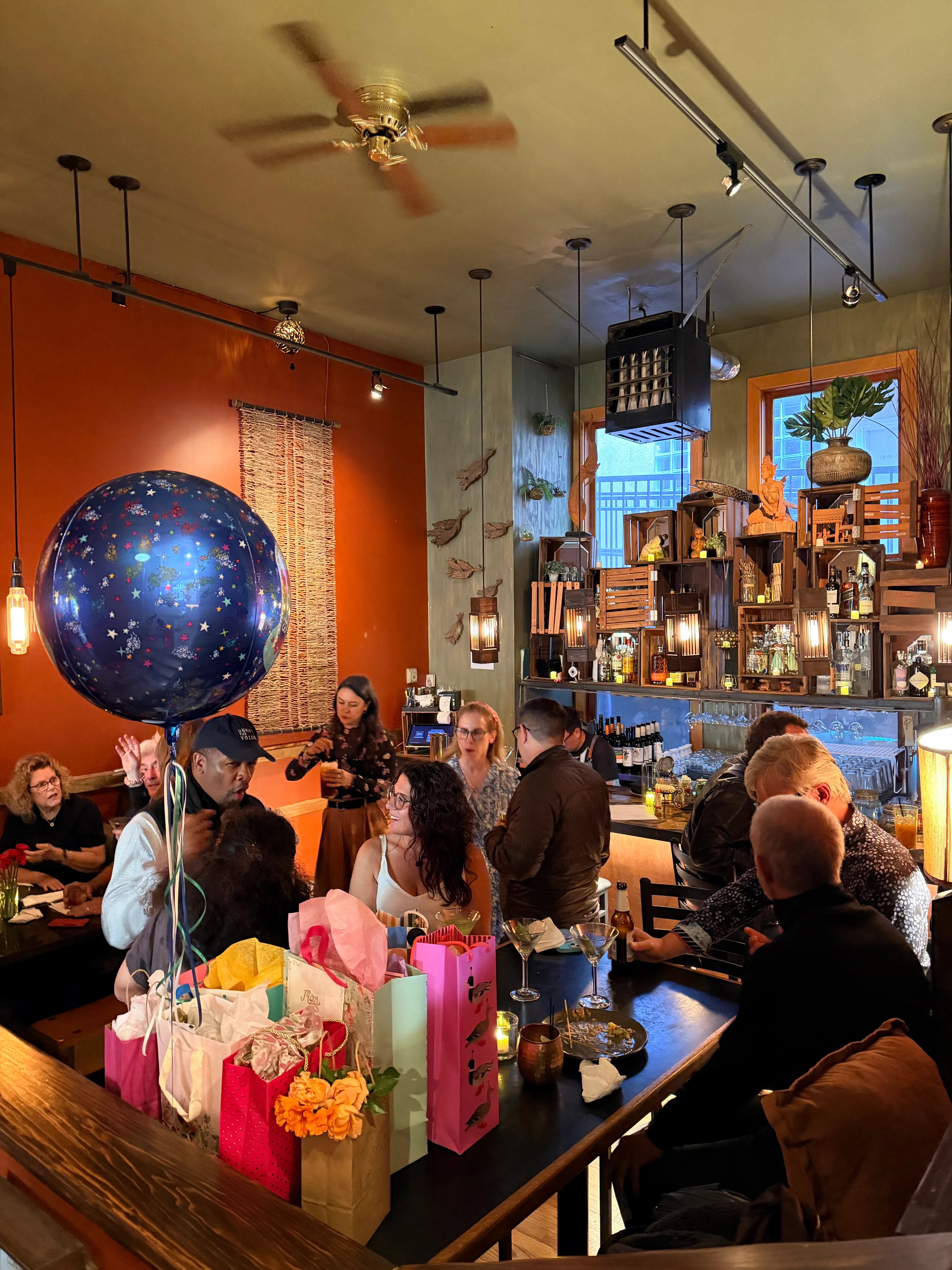 Busy restaurant bar interior with colorful balloon, warm lighting, and dining guests