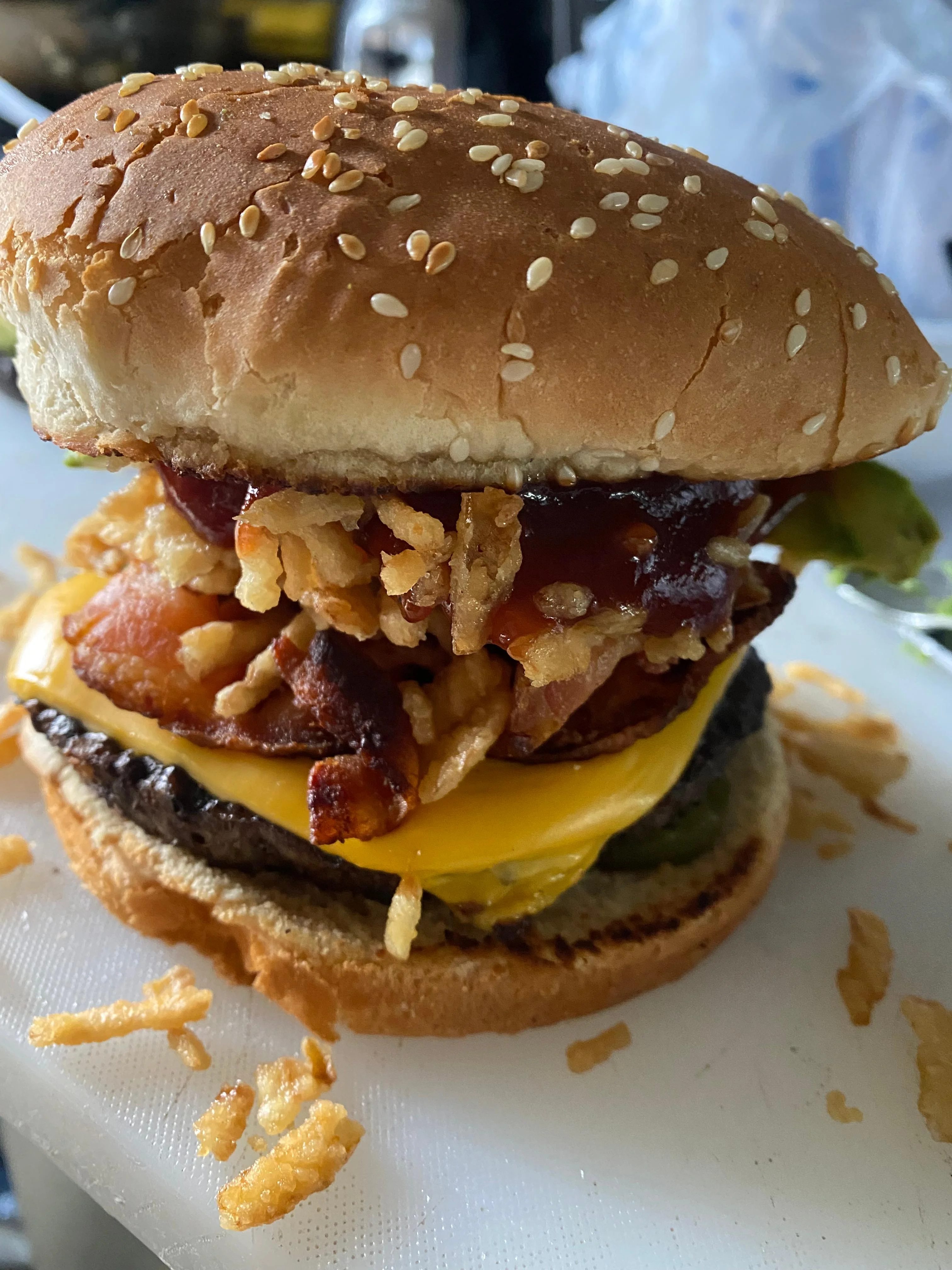 A large hamburger with a sesame seed bun, filled with layers of bacon, cheese, crispy onions, and barbecue sauce.