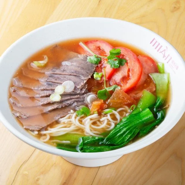 Bowl of tomato beef noodle soup garnished with herbs and spices