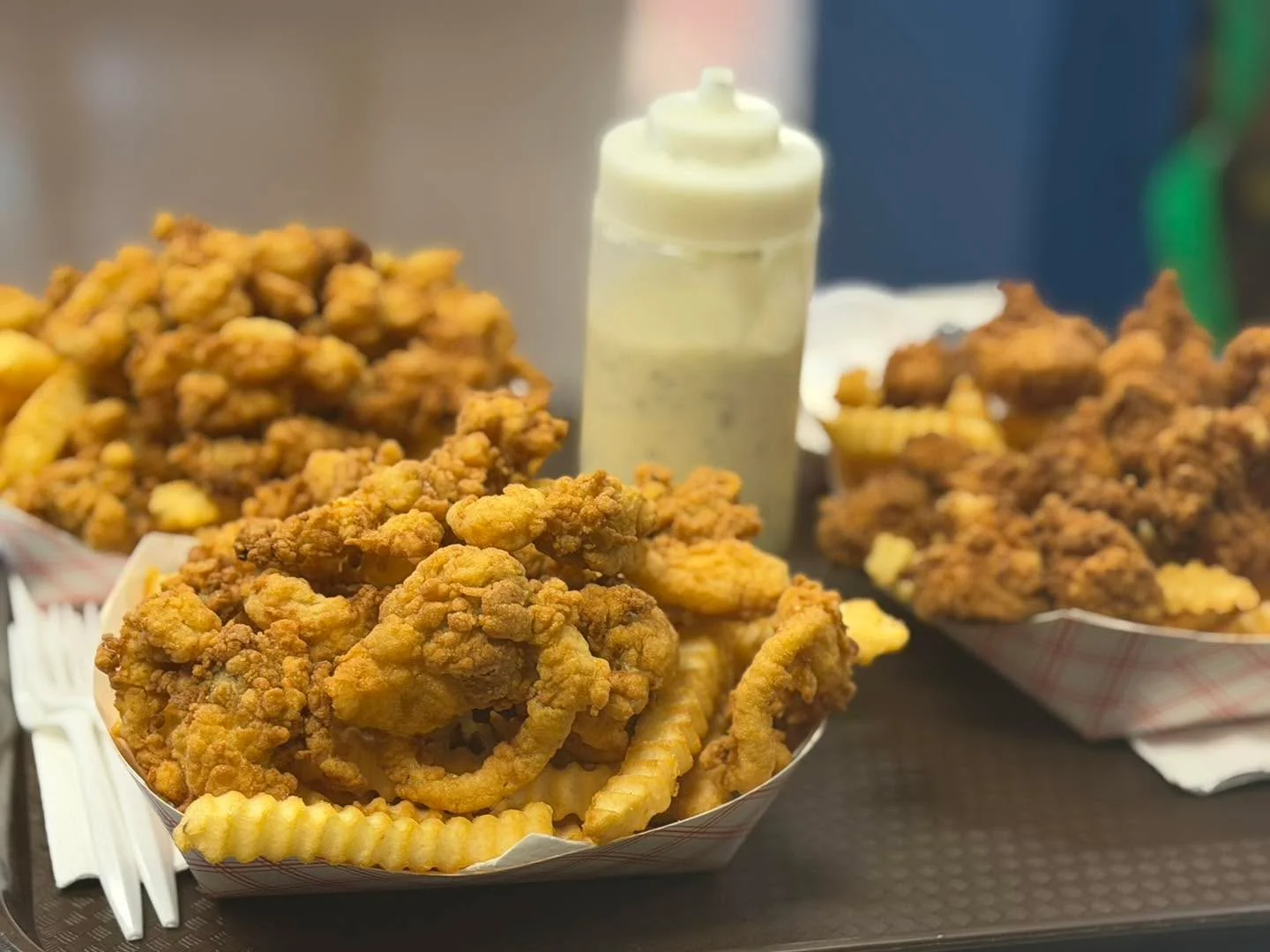 A serving of crispy fried chicken accompanied by crinkle-cut fries. A container of dipping sauce is visible in the background.