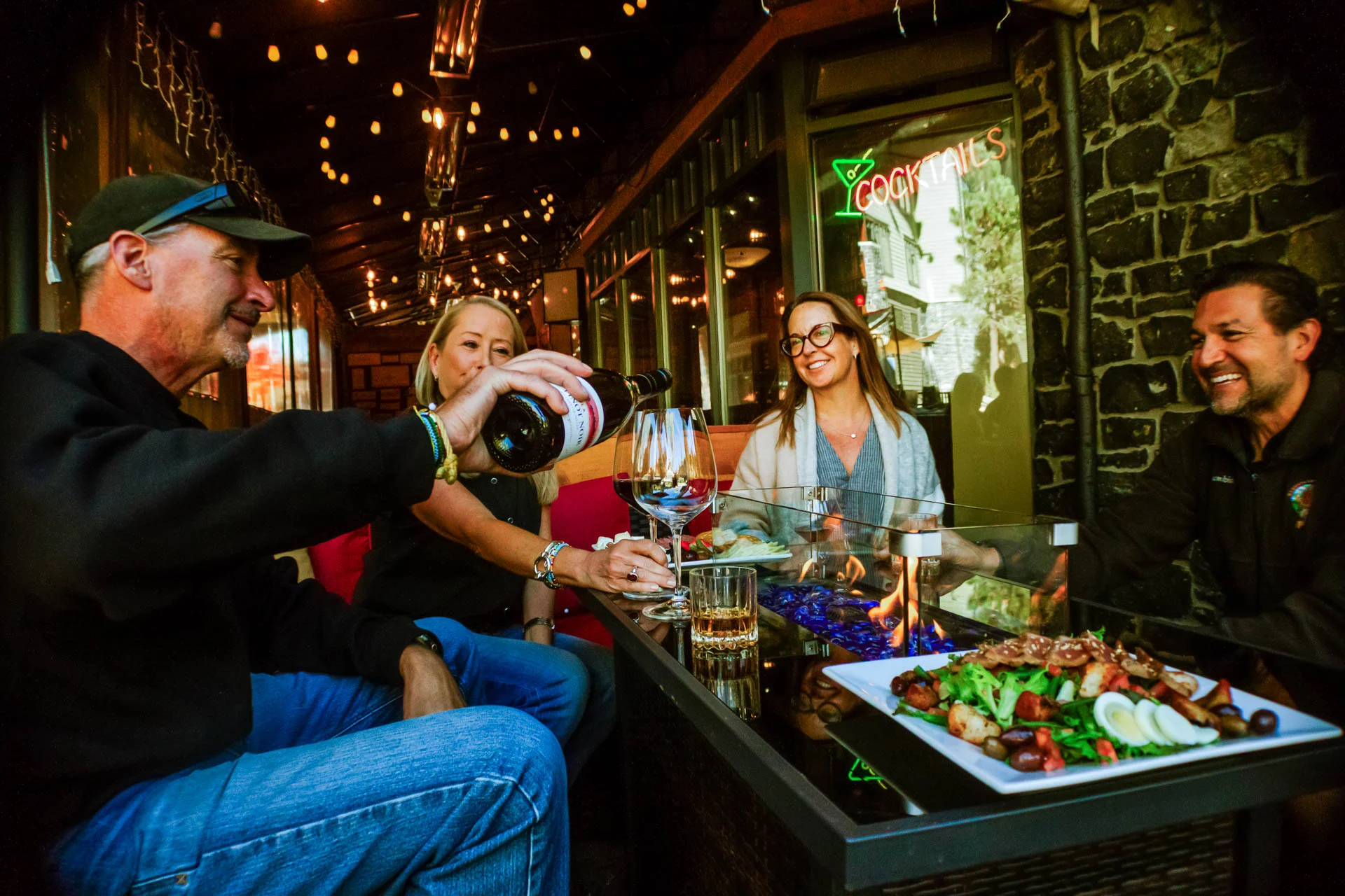 A group of friends enjoying wine and food together by a cozy fireplace at Side Door Wine Bar & Café, highlighting the welcoming atmosphere.