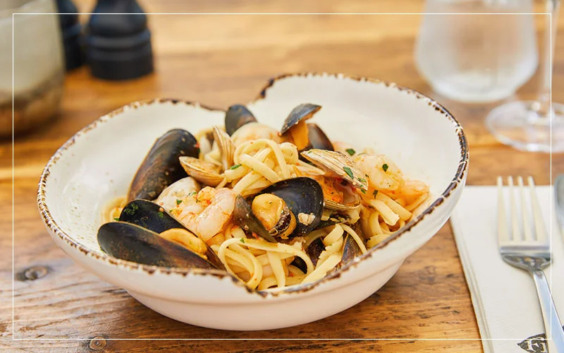 A bowl of linguine with shrimp, mussels, and clams on a wooden table.