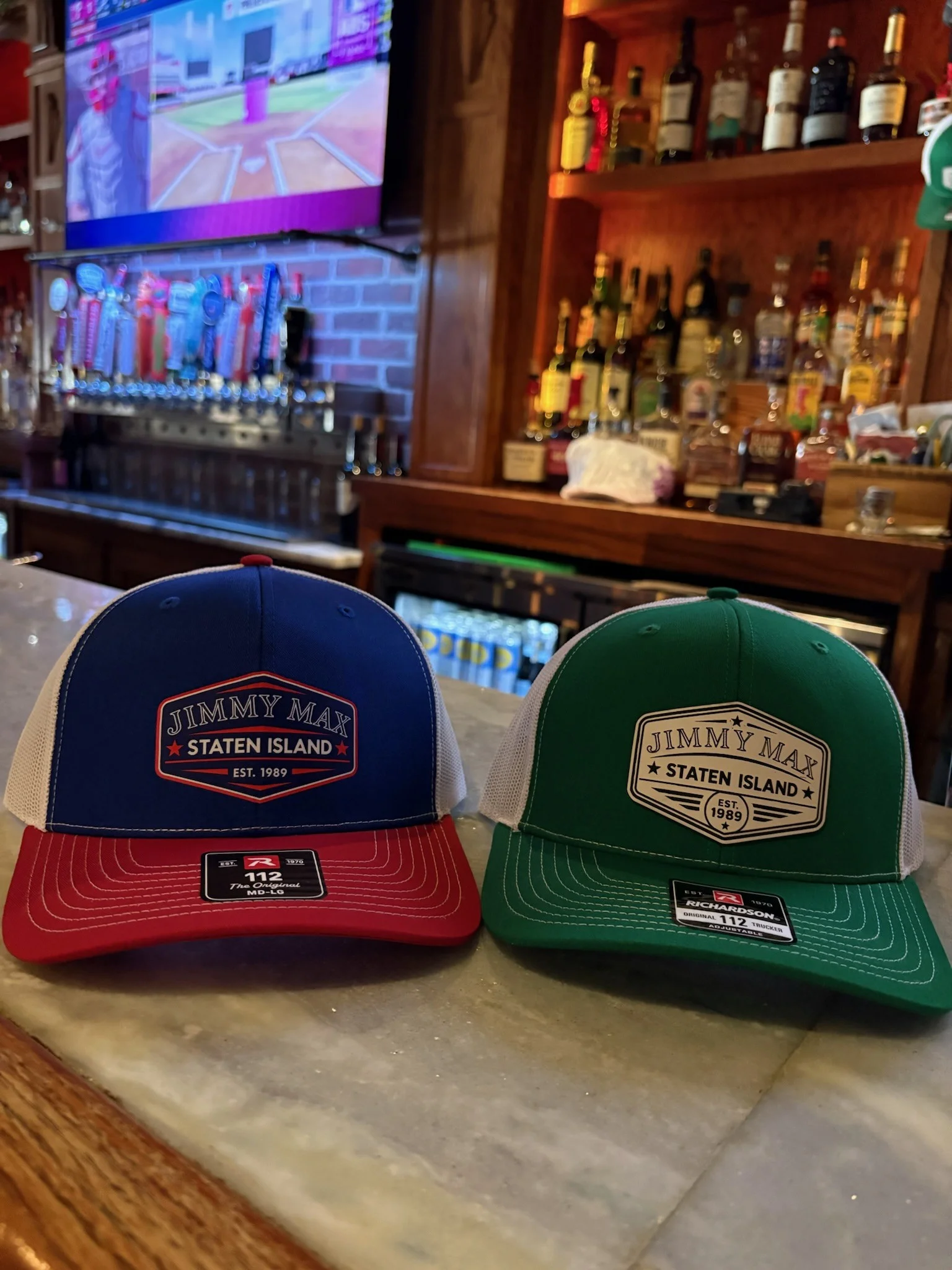 Branded trucker hats displayed on a restaurant bar beside liquor bottles and beer taps
