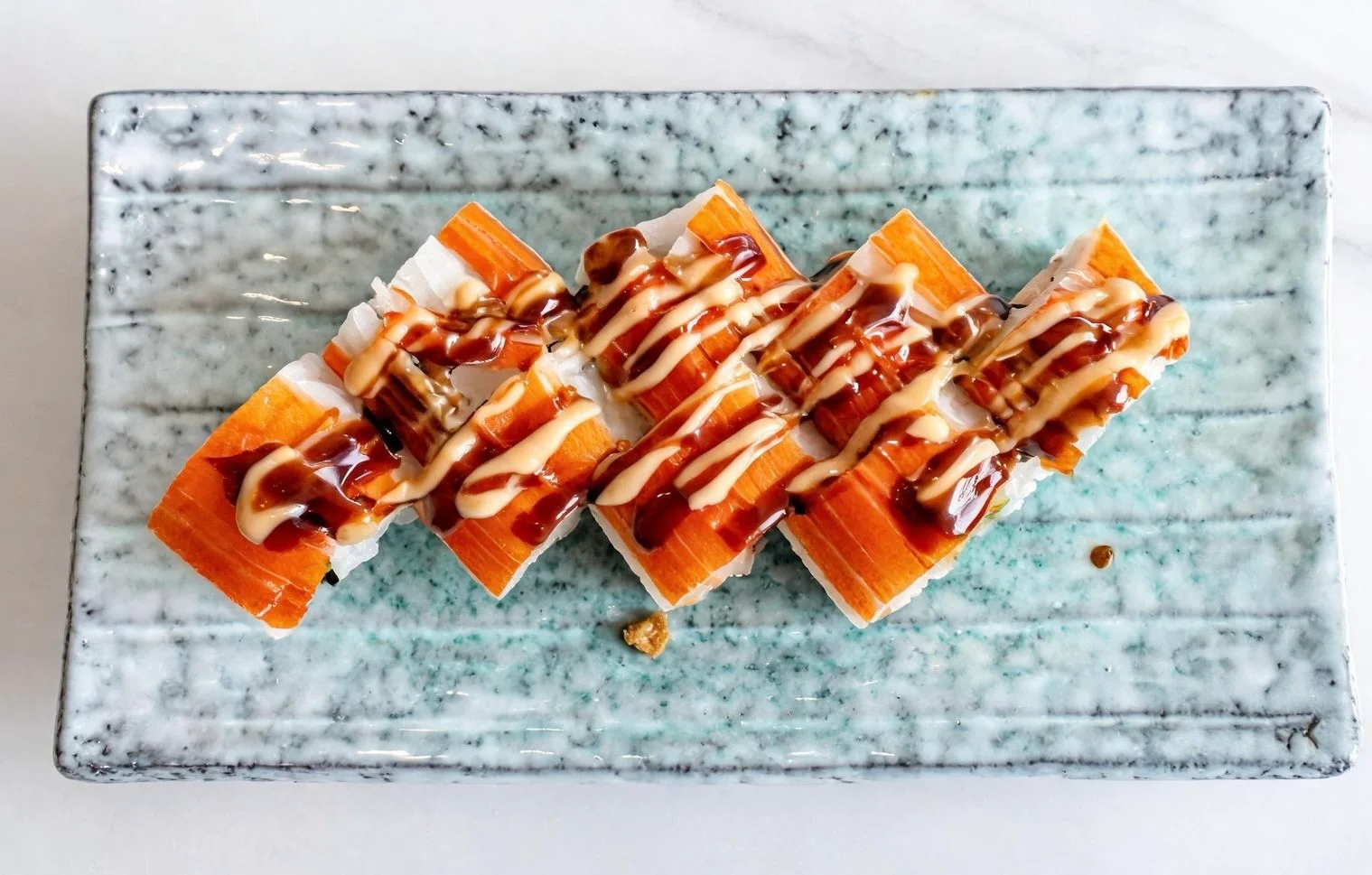 Japanese sushi rolls drizzled with sauce on a decorative plate