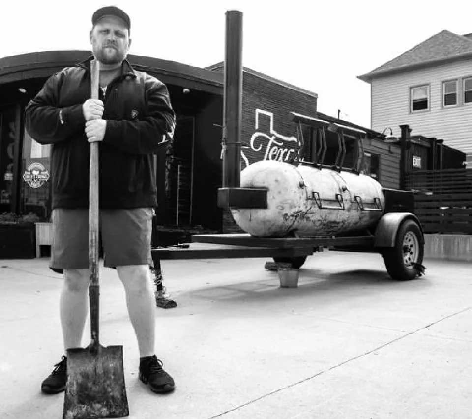 Barbecue chef with shovel beside a smoker trailer
