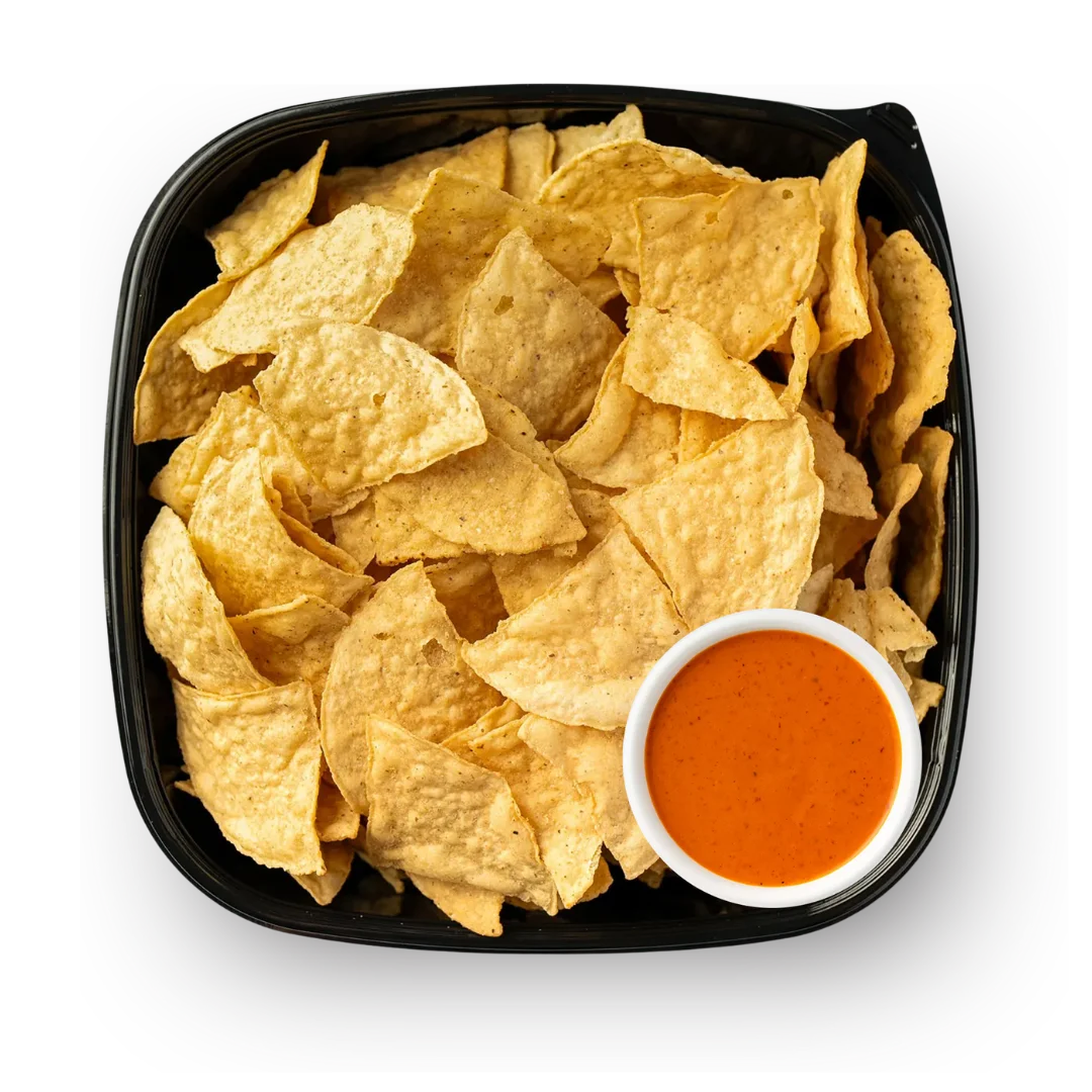 Tortilla chips served in a round basket lined with parchment paper, accompanied by two small clear cups containing guacamole and fresh salsa (pico de gallo).
