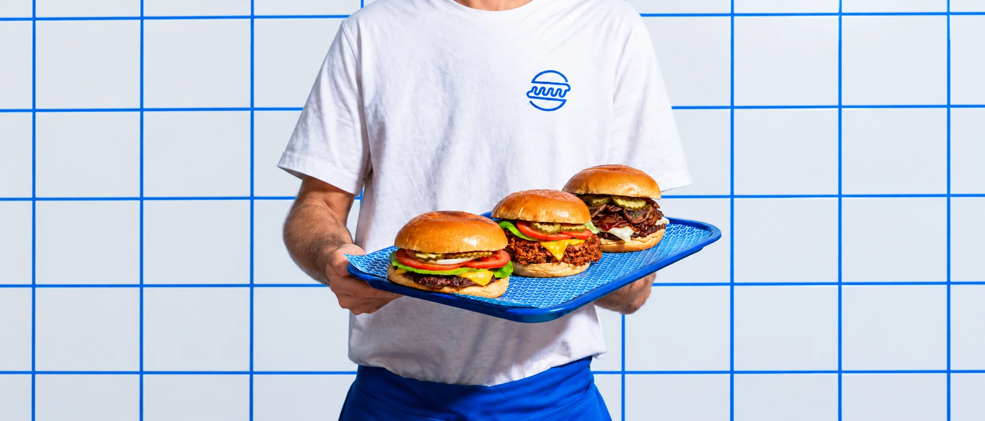 Three gourmet burgers served on a blue tray against a tiled backdrop