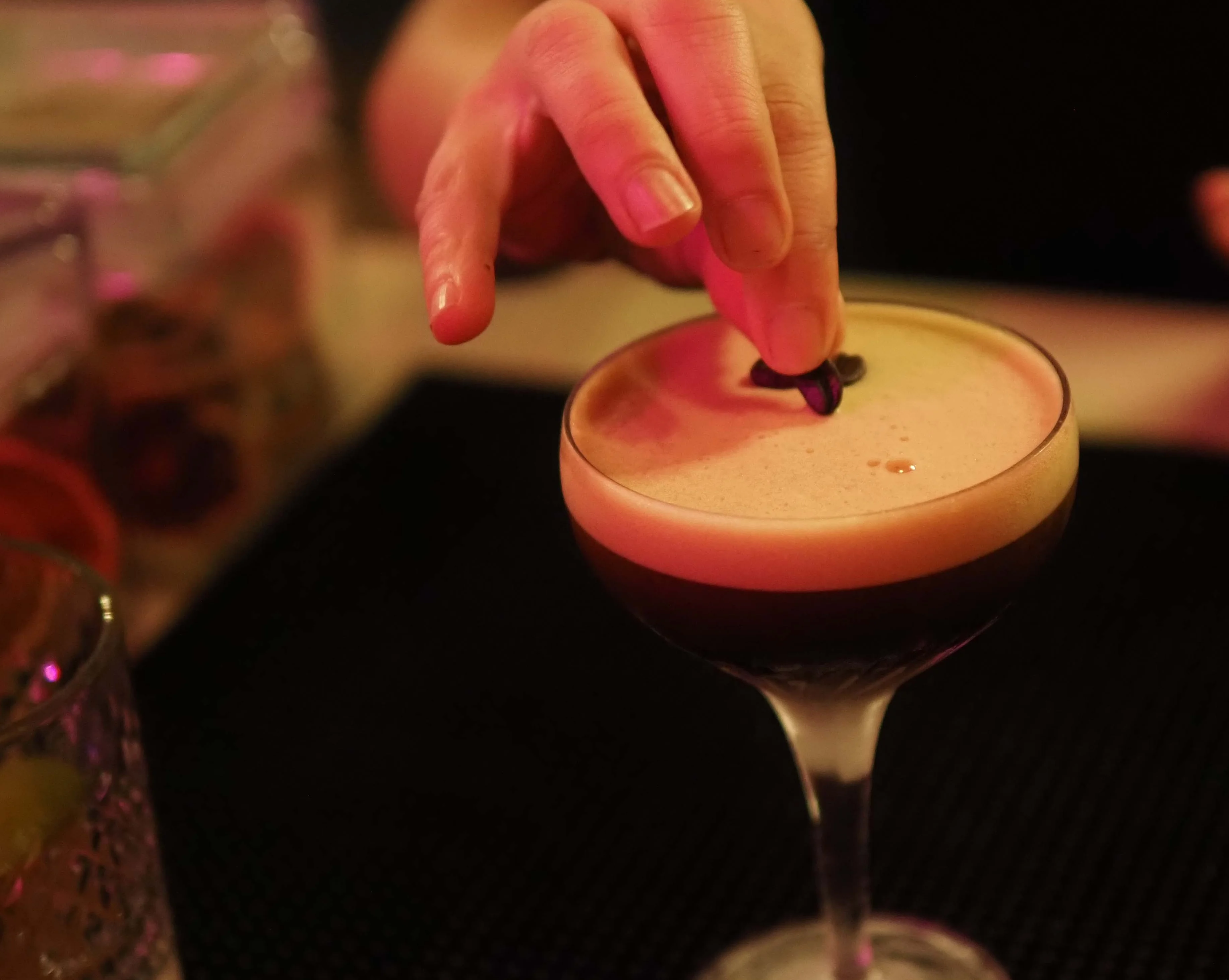 Bartender garnishing an espresso martini with coffee beans