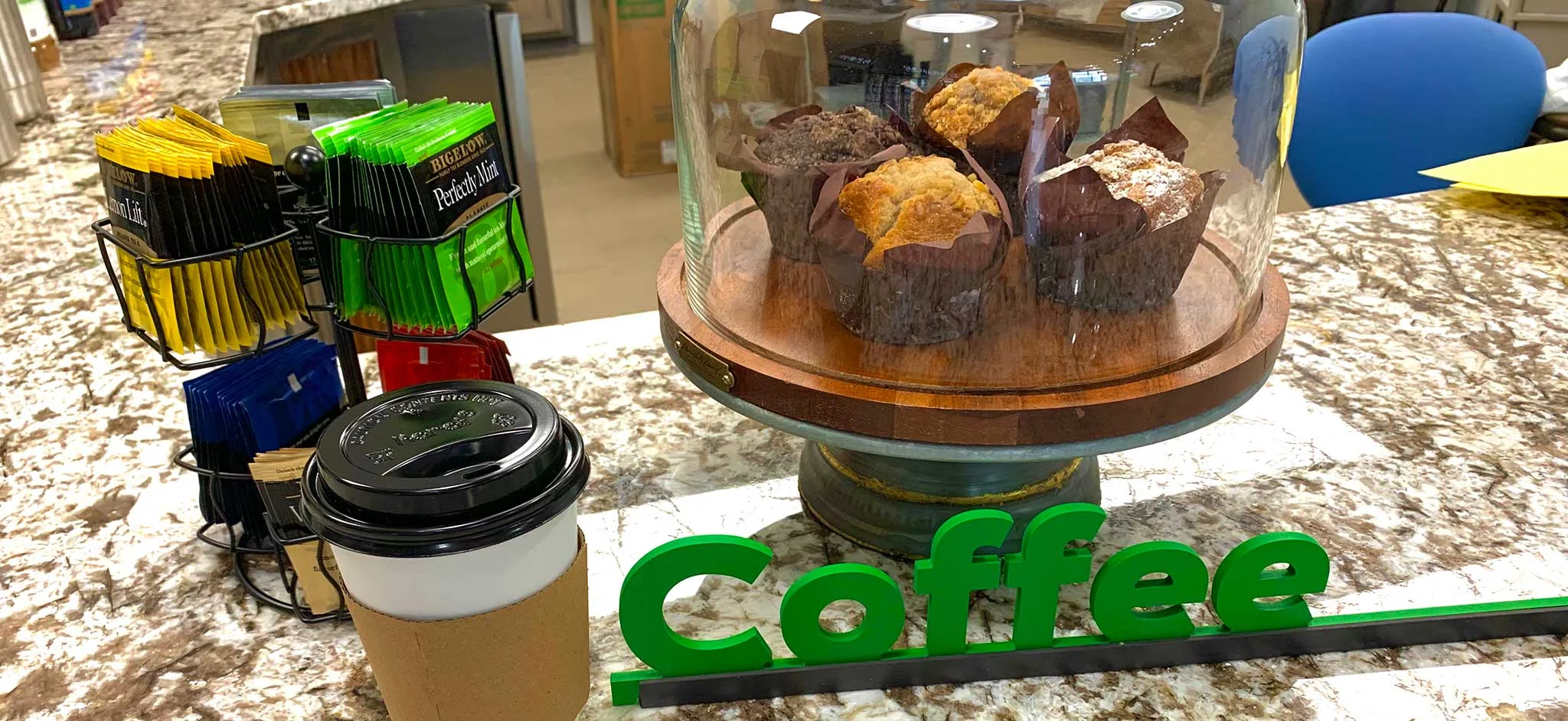 Freshly baked muffins displayed under a glass dome with coffee