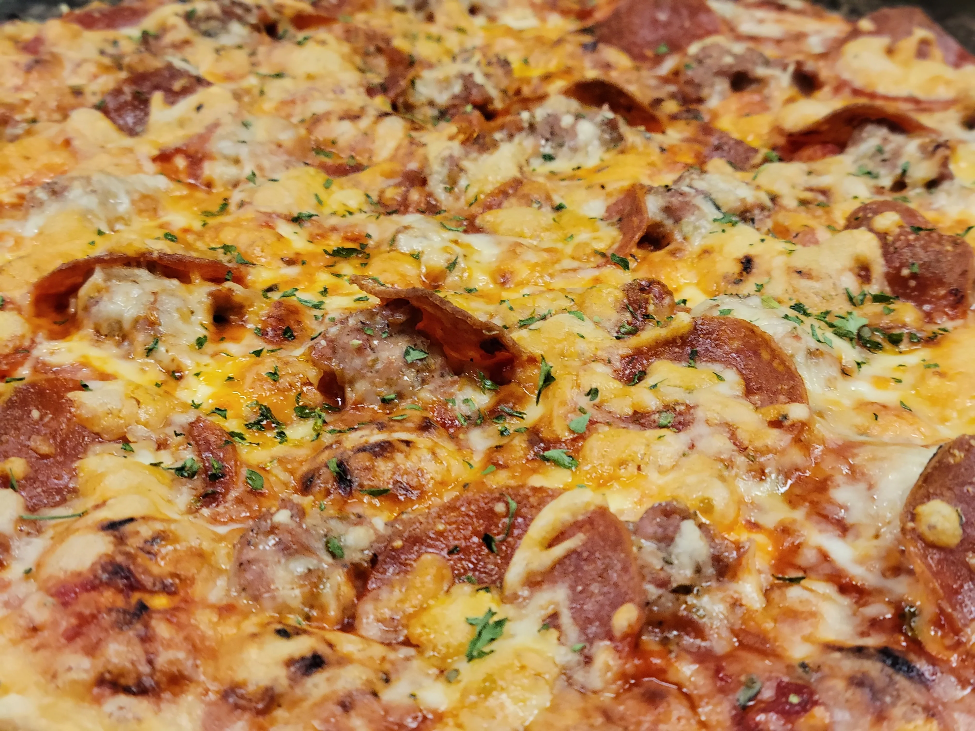 A freshly baked pizza topped with pepperoni, sausage, and melted cheese, garnished with herbs.