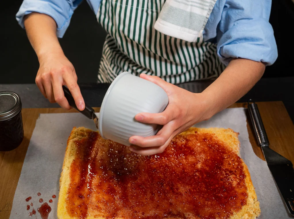 Baker spreading jam on a sponge cake
