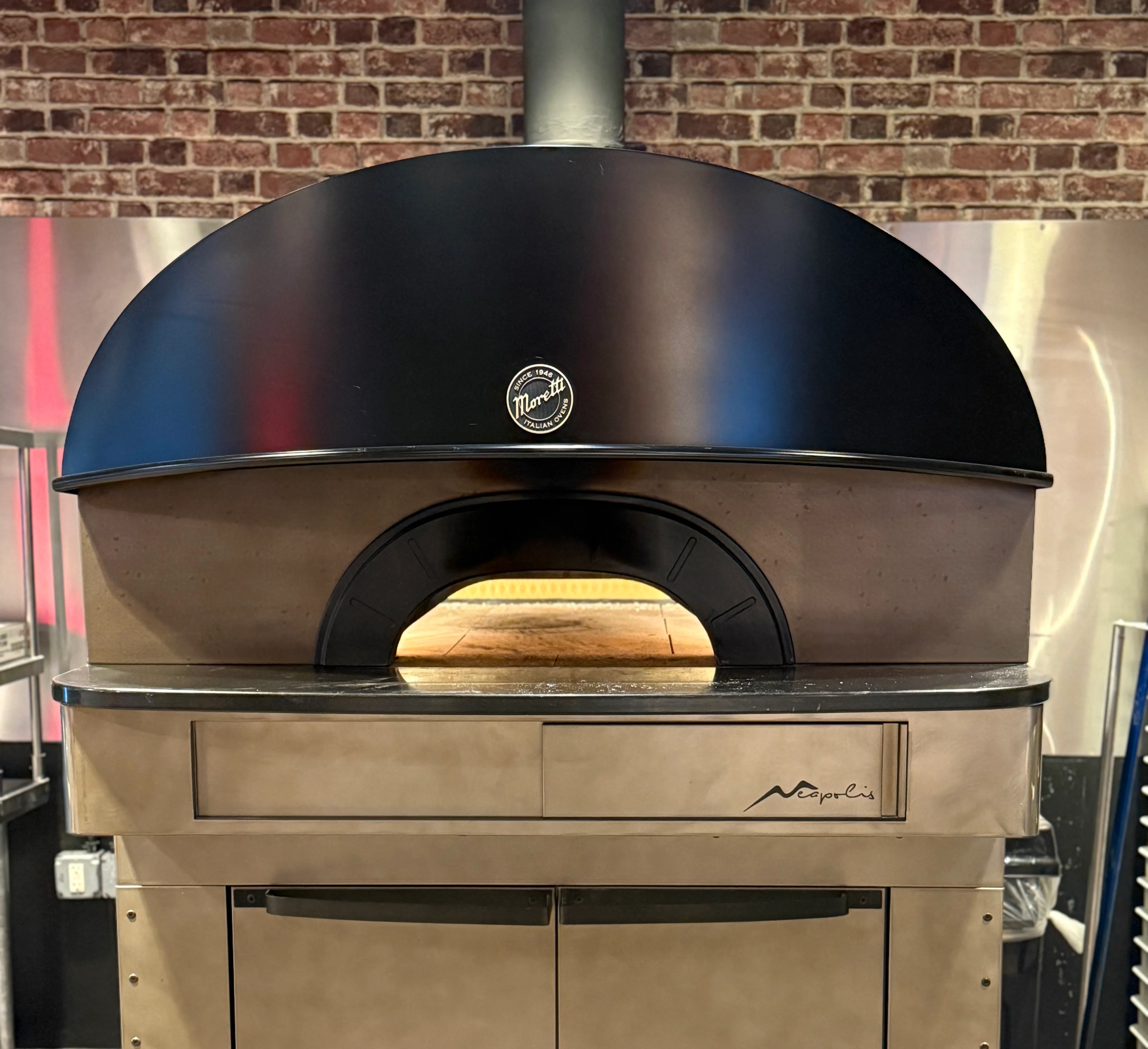 Wood-fired pizza oven with black dome and brick backdrop