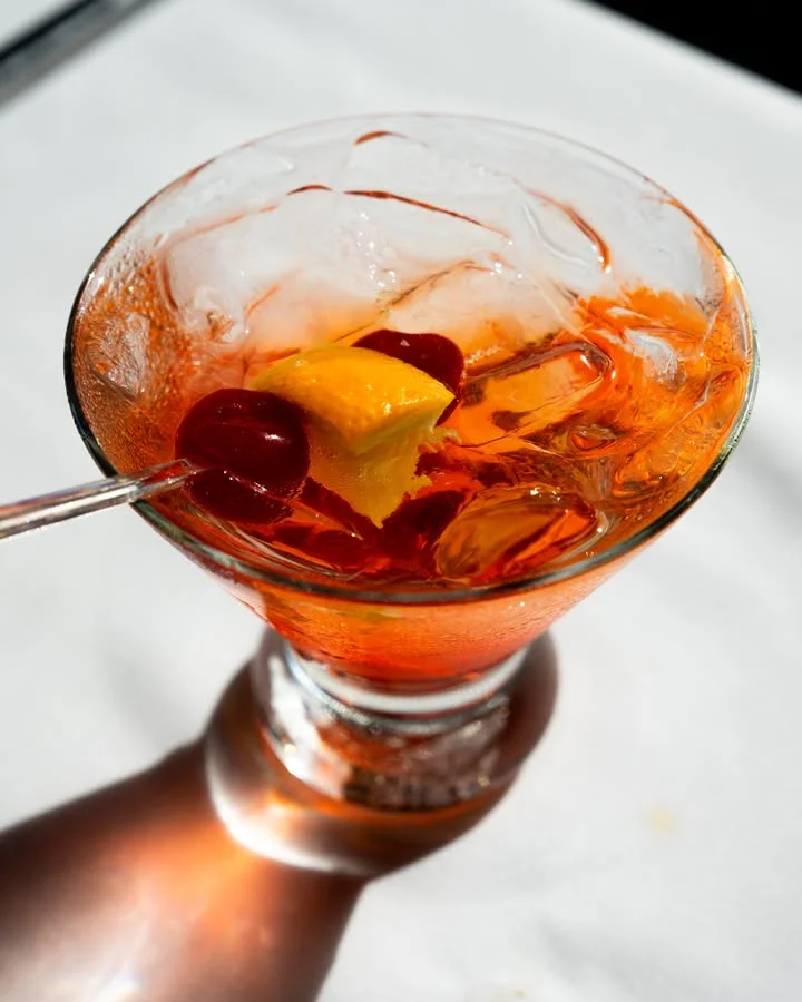 A vibrant cocktail in a glass filled with ice, garnished with a cherry and a piece of fruit.