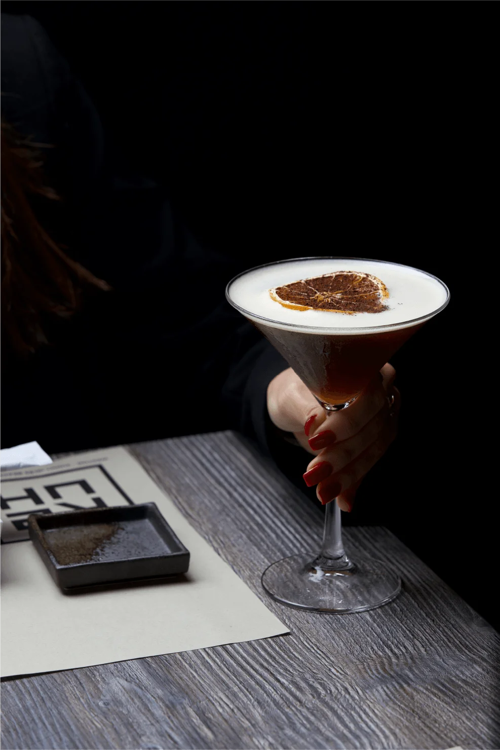 An espresso martini style cocktail with a foamy top and a dried citrus wheel garnish