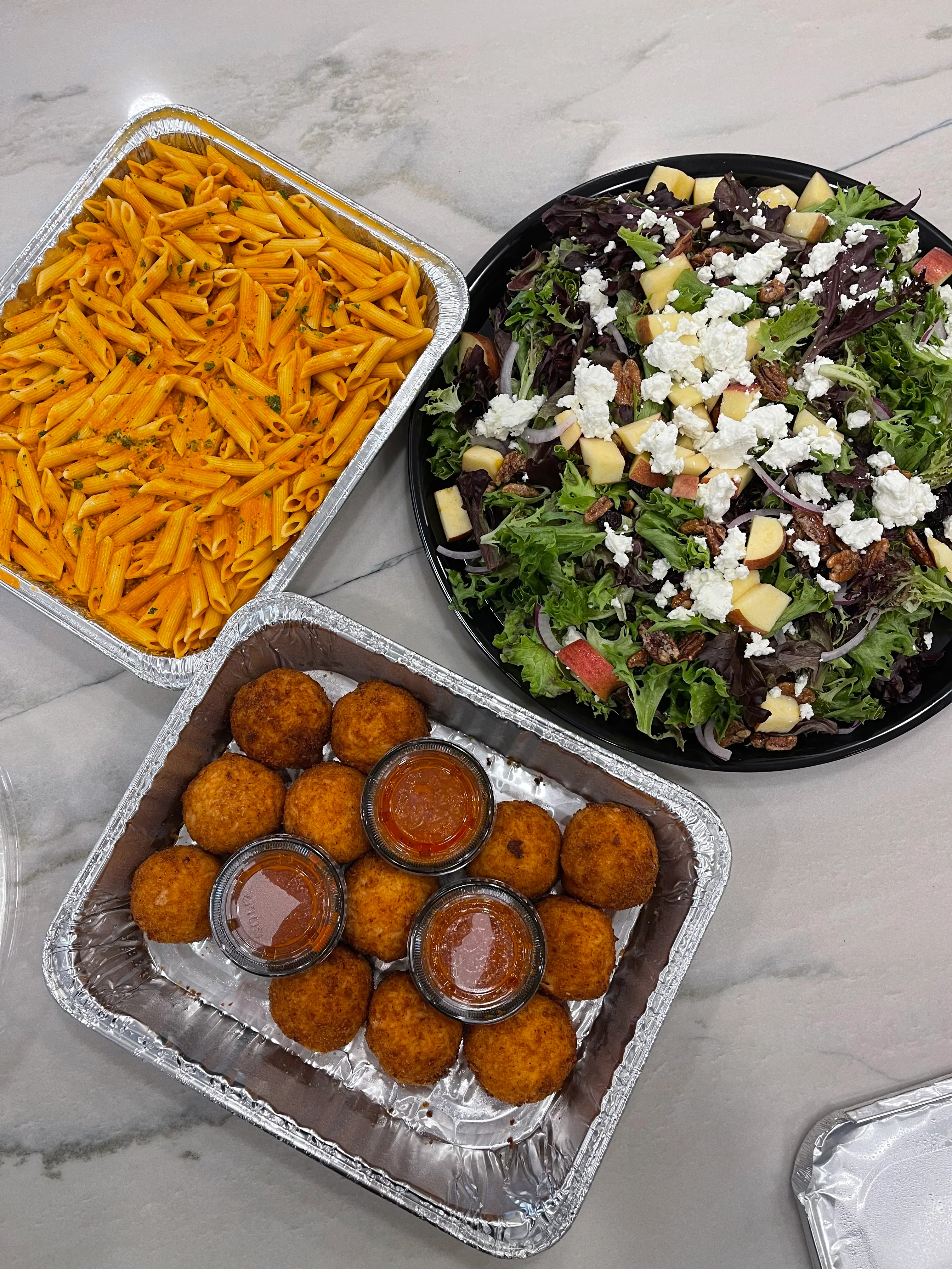 Pasta, salad, and fried balls with sauces in takeout containers.