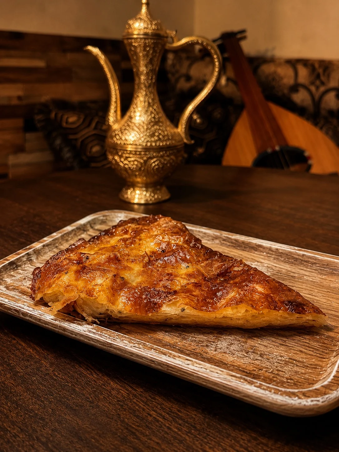 A golden pastry slice on a wooden plate with a decorative teapot in the background.