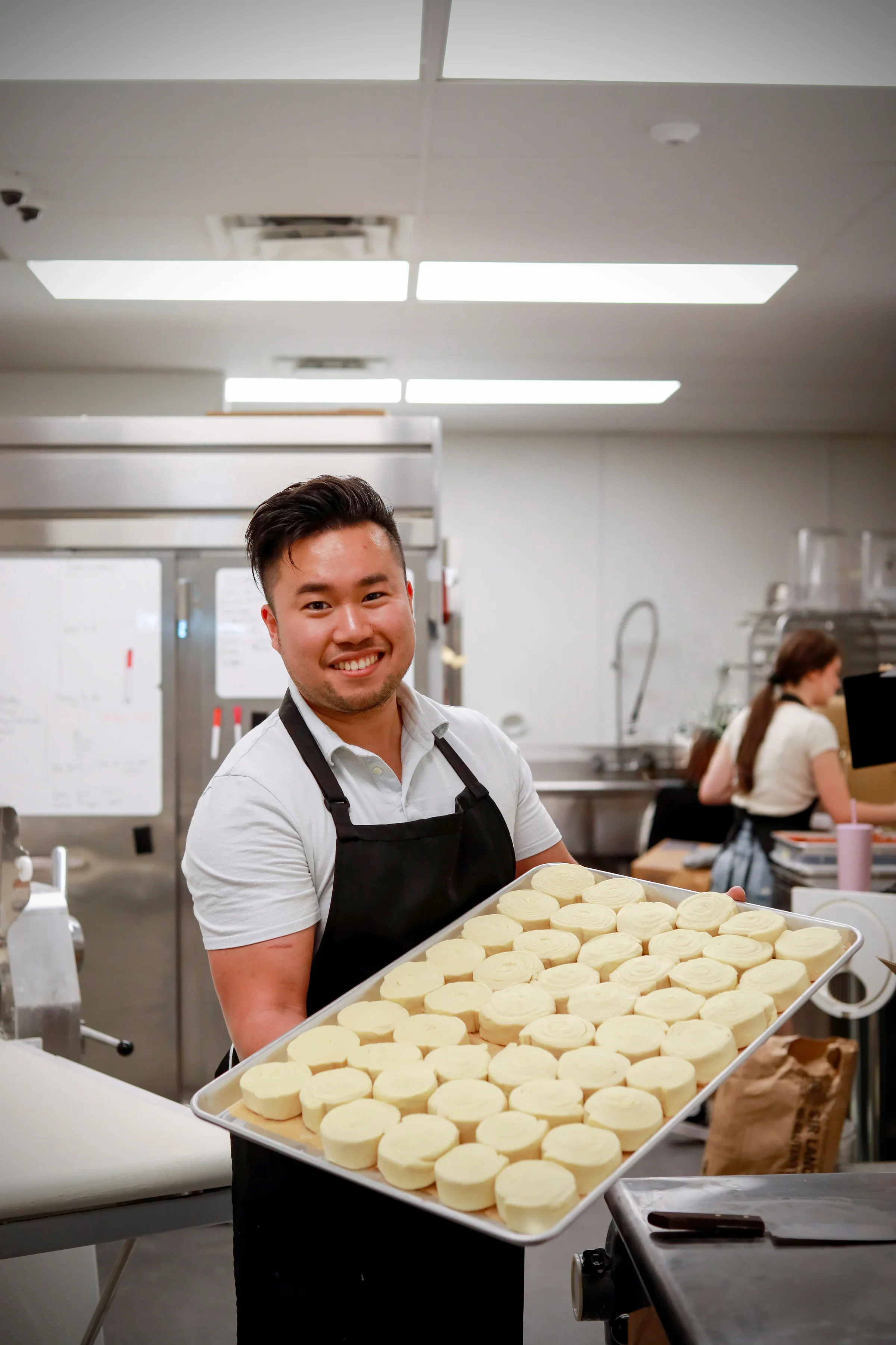 Baker holding freshly made cinnamon rolls in a commercial kitchen