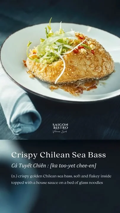 A beautifully plated dish of crispy Chilean sea bass, garnished with fresh greens and served on a bed of glass noodles. The fish is golden and flaky, topped with a flavorful house sauce.