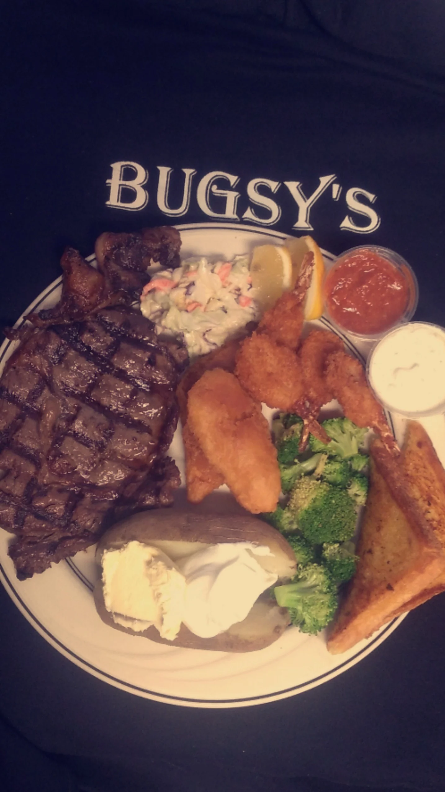 A hearty meal featuring a grilled steak, fried shrimp, coleslaw, and a baked potato, all served on a circular plate.