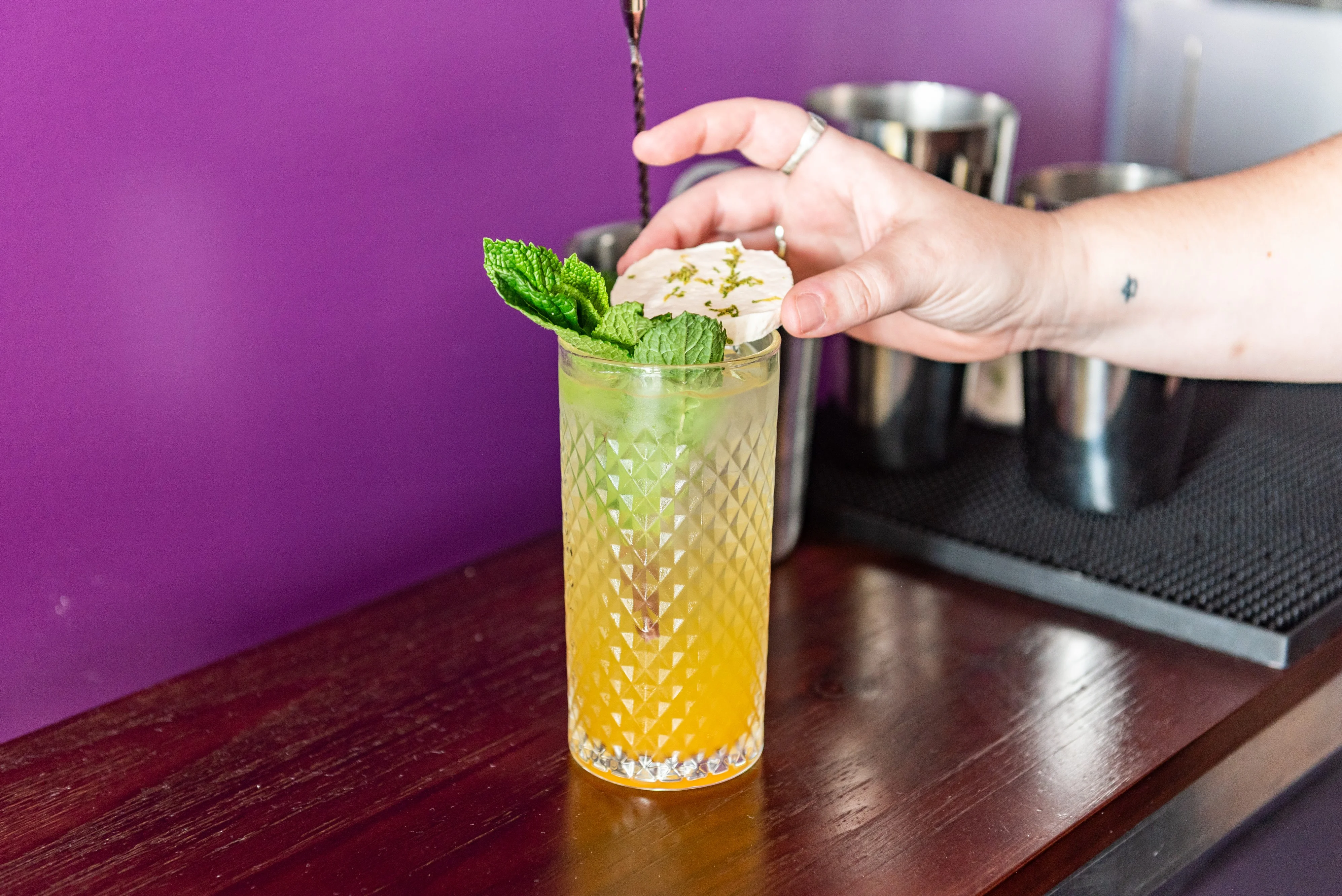 A vibrant cocktail garnished with fruit and herbs on a wooden table.