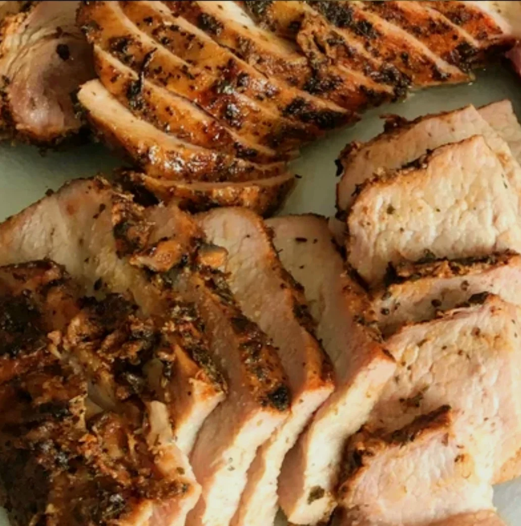 Sliced roasted pork, showcasing a crispy outer layer and tender meat, arranged neatly on a surface.