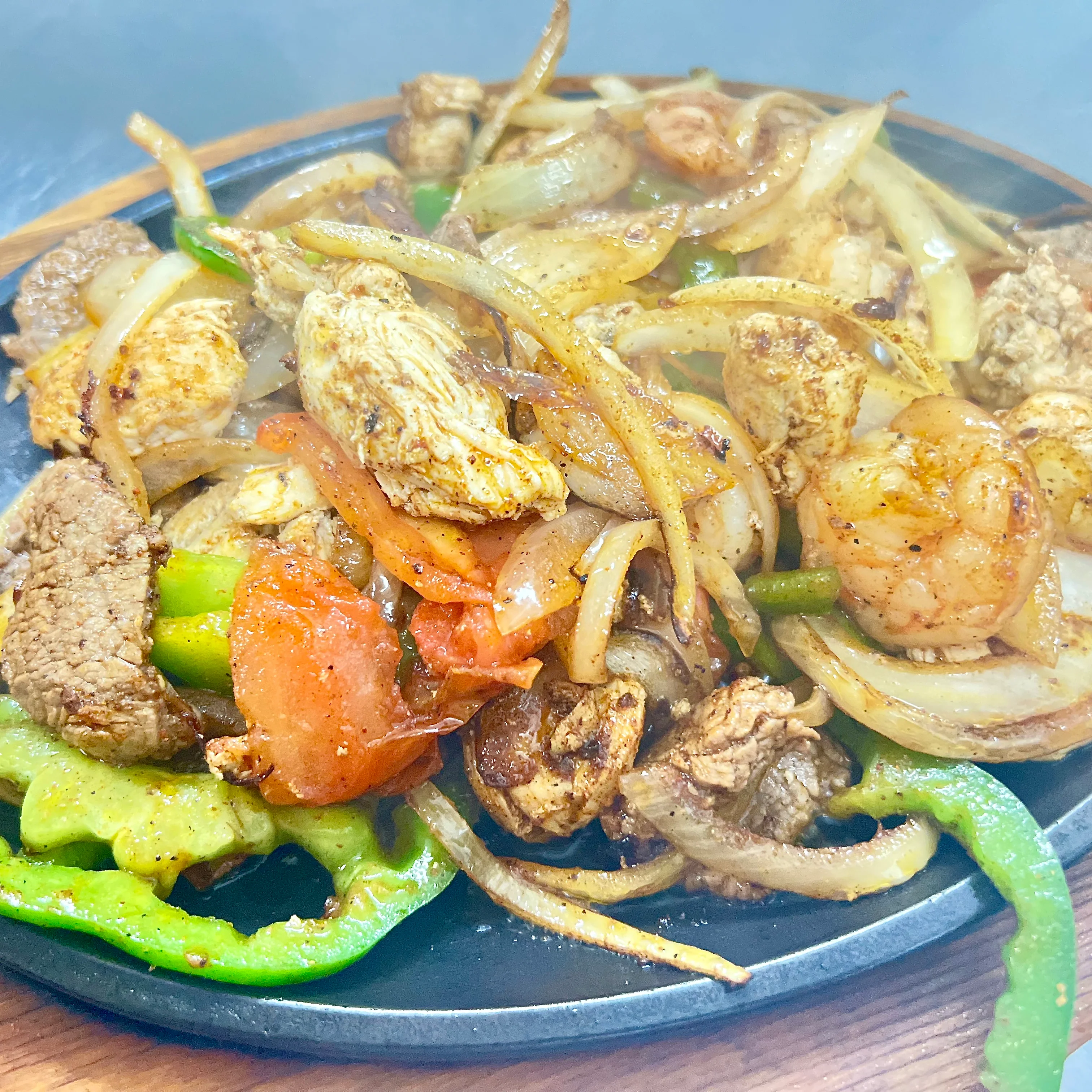 Sizzling fajitas with chicken, beef, and shrimp on a hot skillet