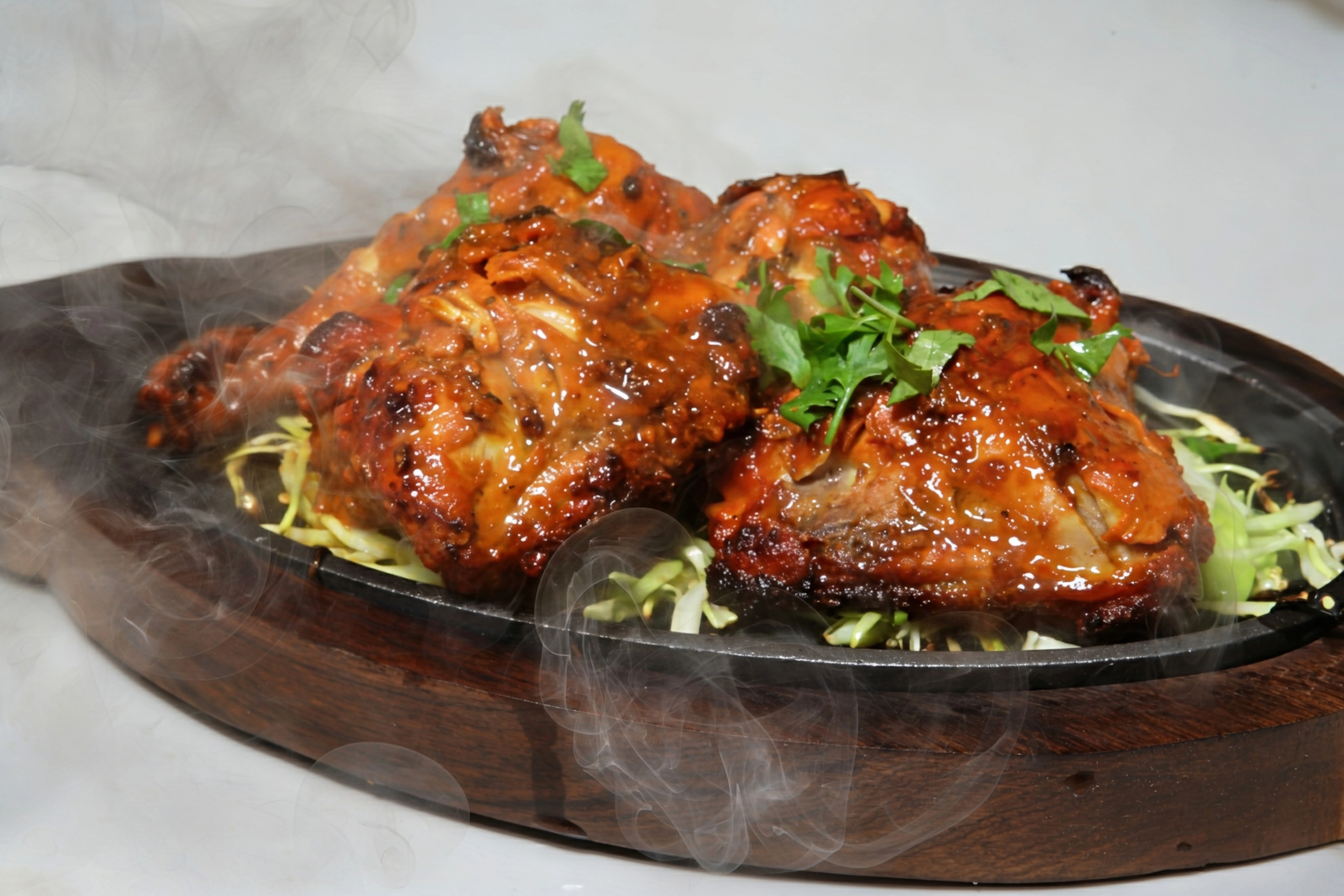 Sizzling grilled chicken pieces coated in a rich sauce, served on a hot platter with a bed of shredded cabbage and fresh herbs.