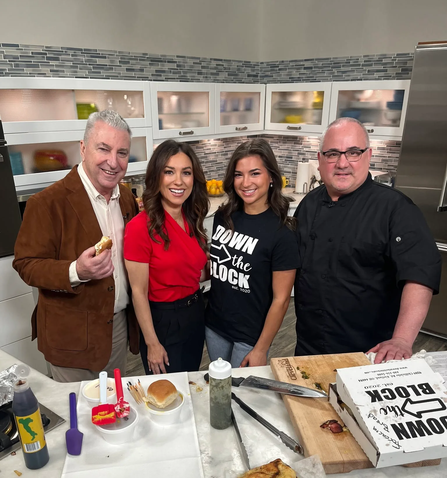 A group of four people gathered in a kitchen setting, preparing food with various utensils and dishes laid out on the counter.